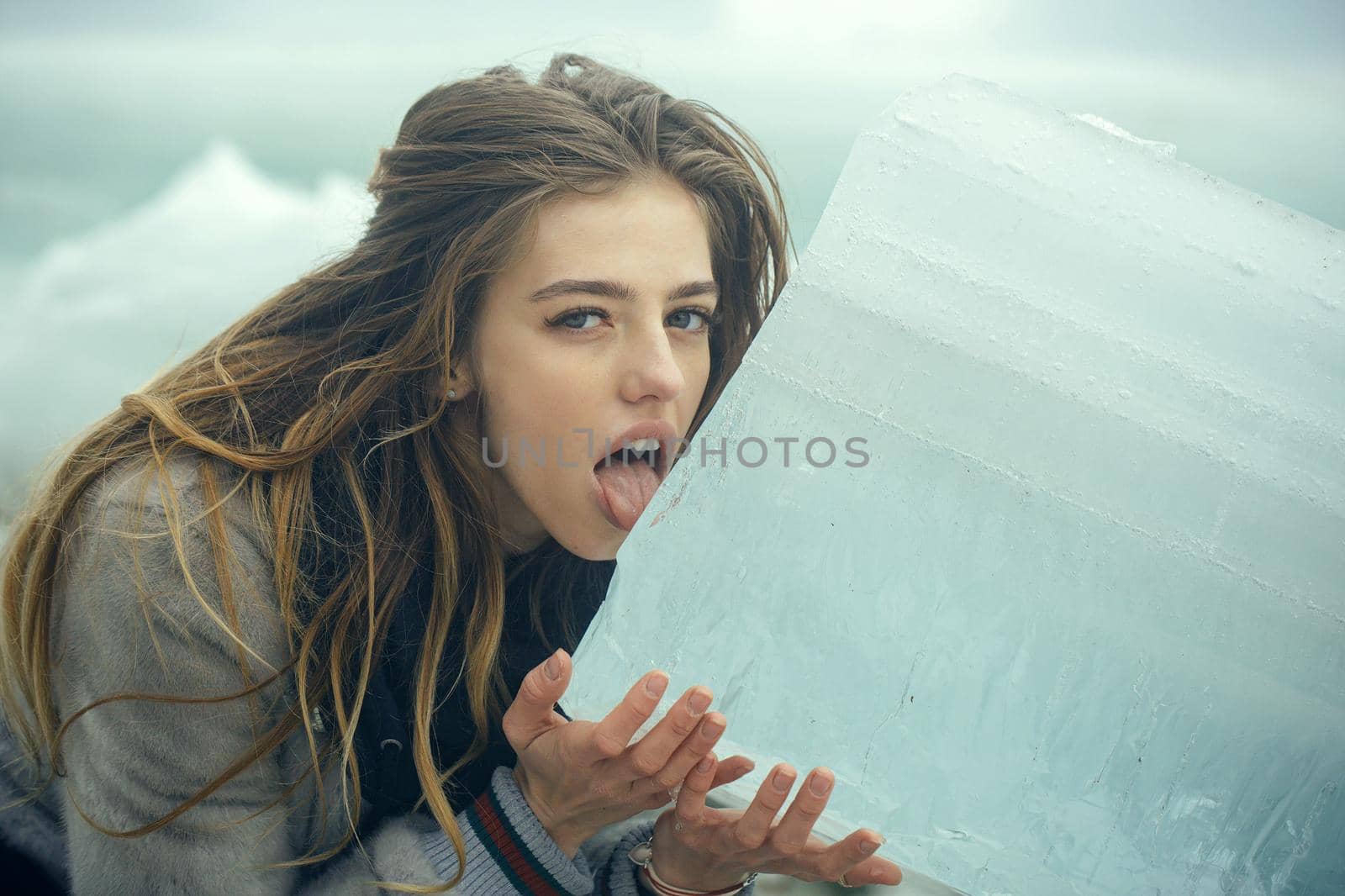 Woman with pretty face lick ice. Girl with frozen hummock. Cold weather. Cracked ice background.