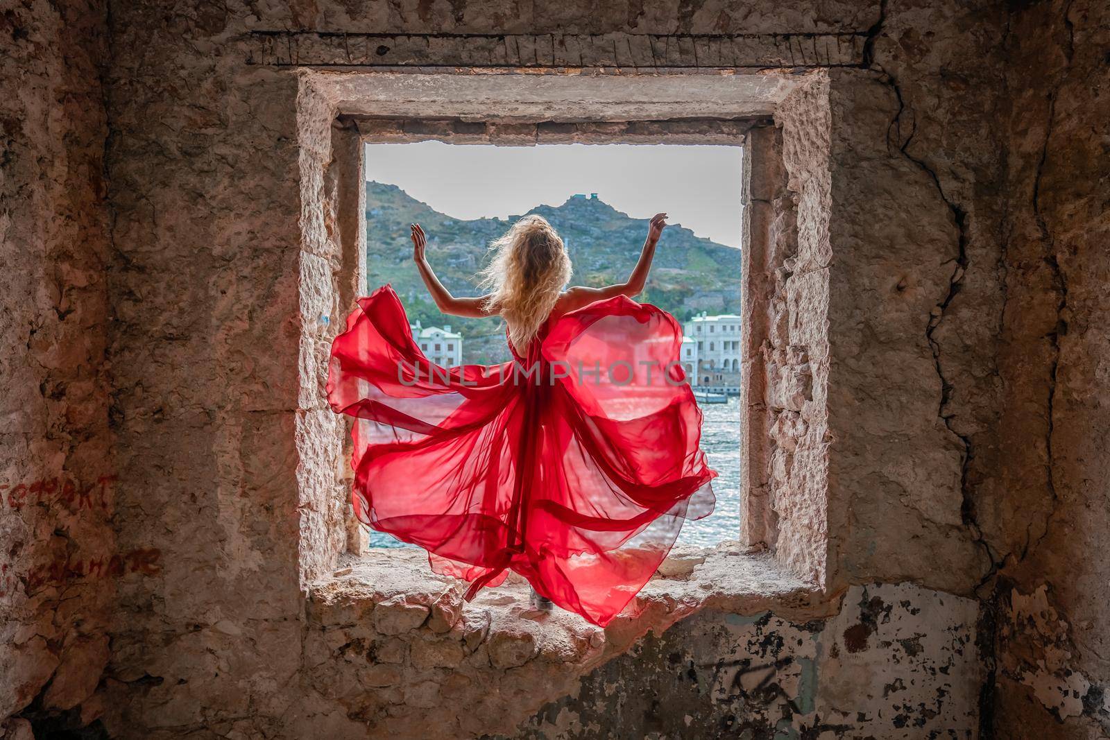 View of Balaklava Bay through an arched balcony in oriental style. The girl in a long red dress stands with her back. Abandoned mansion on the Black Sea coast by Matiunina