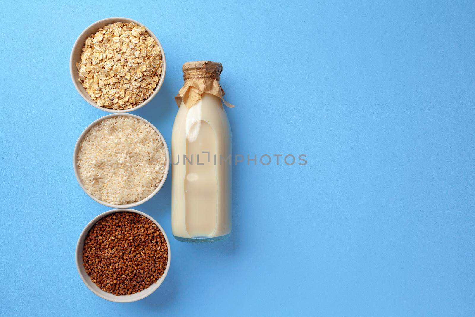 Vegetable milk concept with milk bottle and bowls with grains and nuts on blue background top view