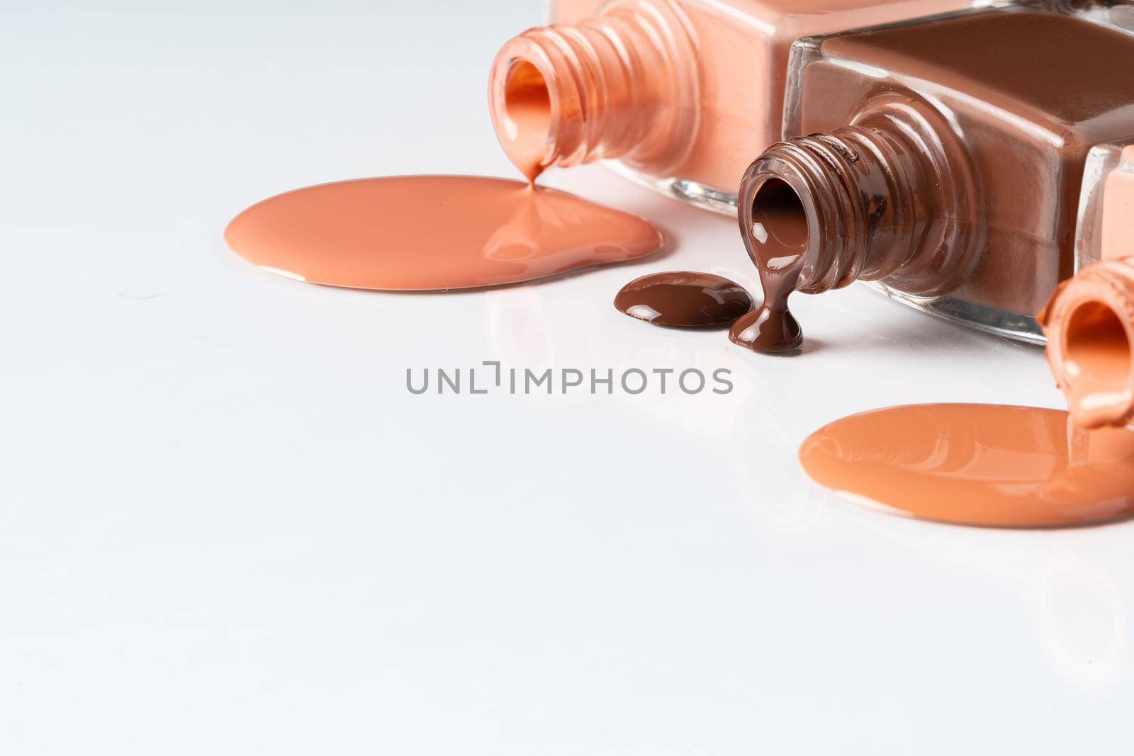 Nude colors nail polish spilled over white background. Close up.