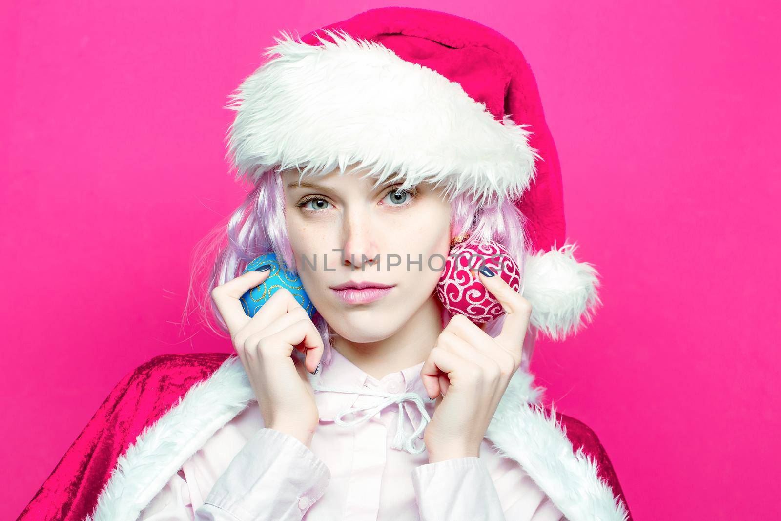 Young woman or cute girl in christmas santa hat holds Christmas balls on pink background. Closeup face portrait.