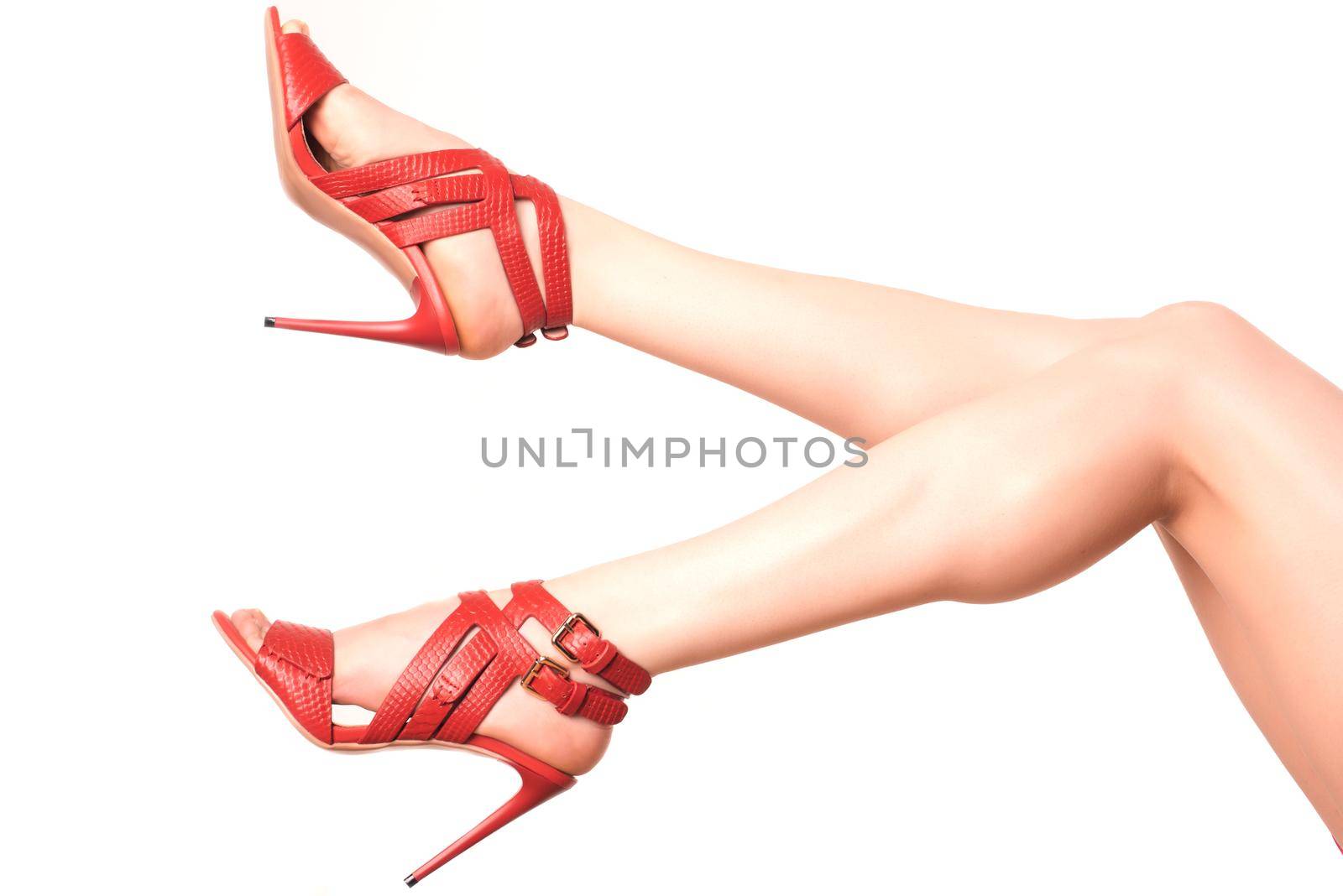 beautiful female legs in red sandals with high heels on a white background.