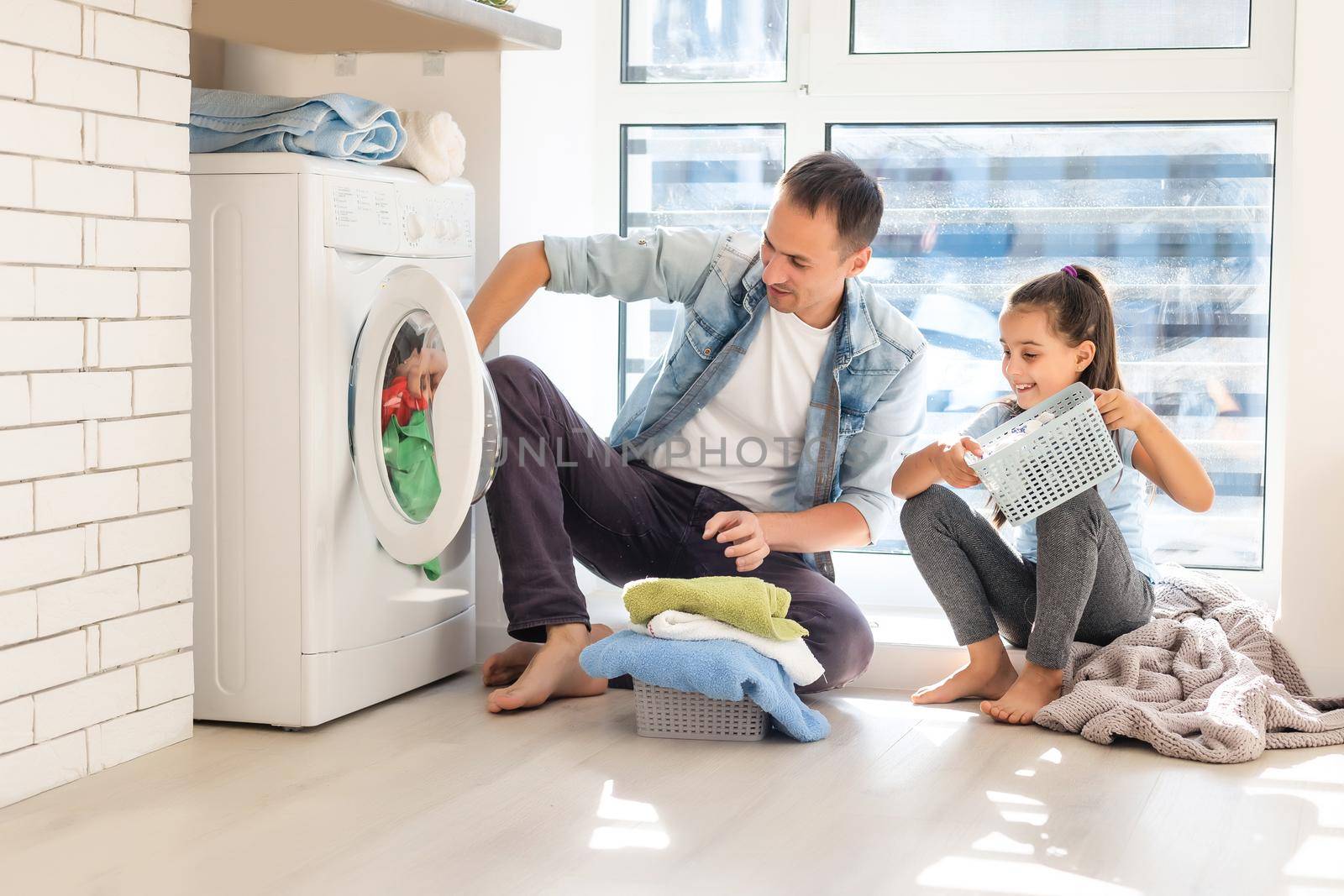 Happy Family loading clothes into washing machine in home by Andelov13