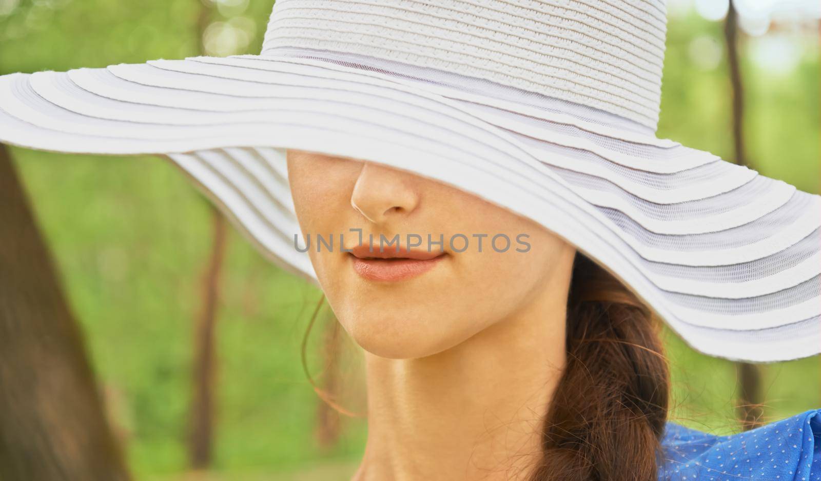 Mysterious woman in hat with wide brim in park in the summer