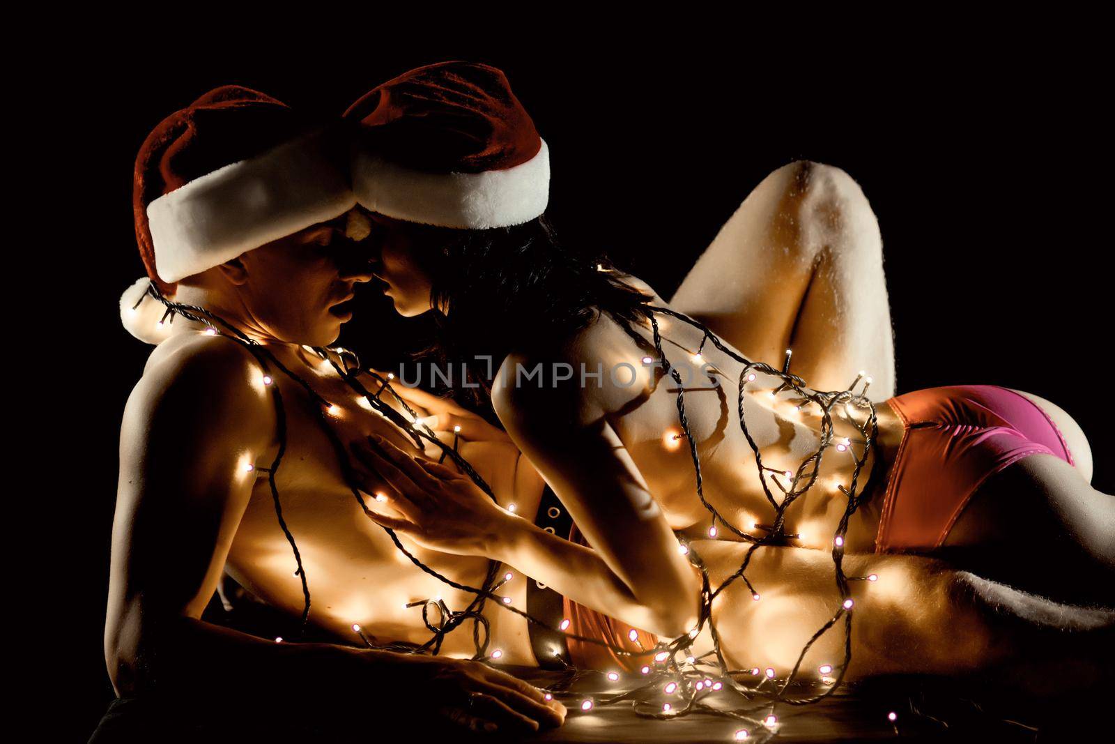 Sexy christmas couple in love. Relations of couple in illuminated garland. Christmas couple in love of sexy man and woman on black by Tverdokhlib