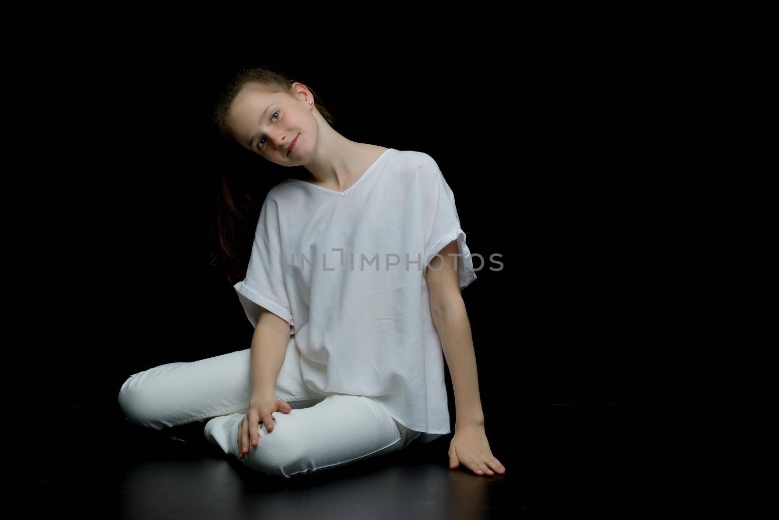 Teen girl teenager sitting on the floor in the studio. The concept of style and fashion. On a black background.
