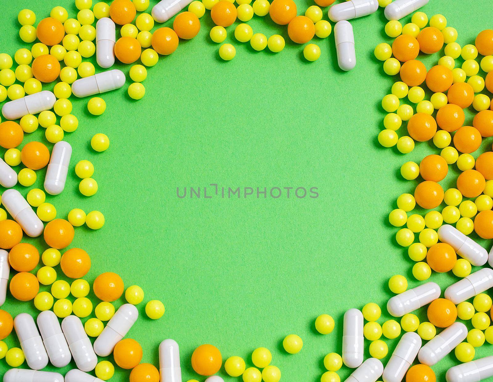 colorful pills for viral diseases in circle frame with copyspace for text. Prevention of influenza, coronavirus, covid-19. yellow, orange vitamins on green background. medical healthcare concept