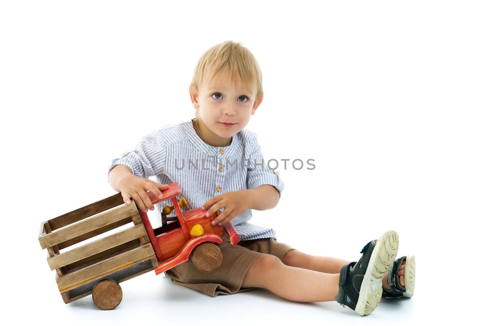 A cute little boy is playing with a big wooden car. The concept of development of a child in a family or a children's center. Advertising of children's goods and services. Isolated on white background.