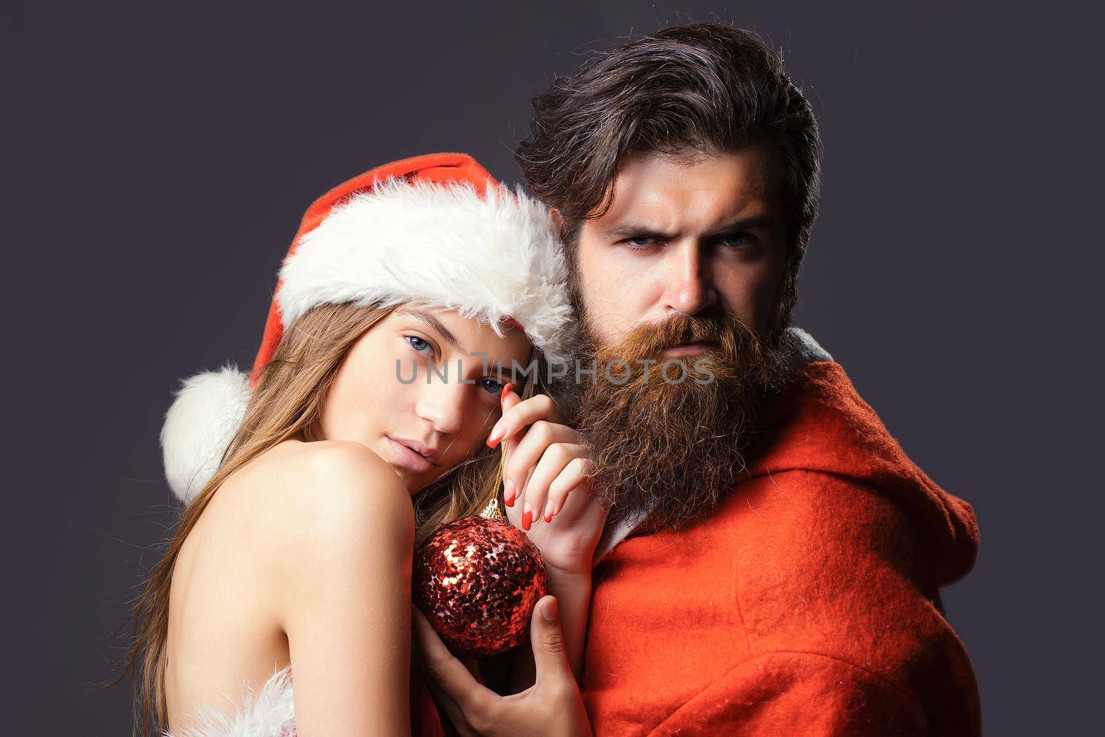 Santa man and pretty young woman in christmas costume and hat on gray background. Sexy christmas couple in love, copy space by Tverdokhlib