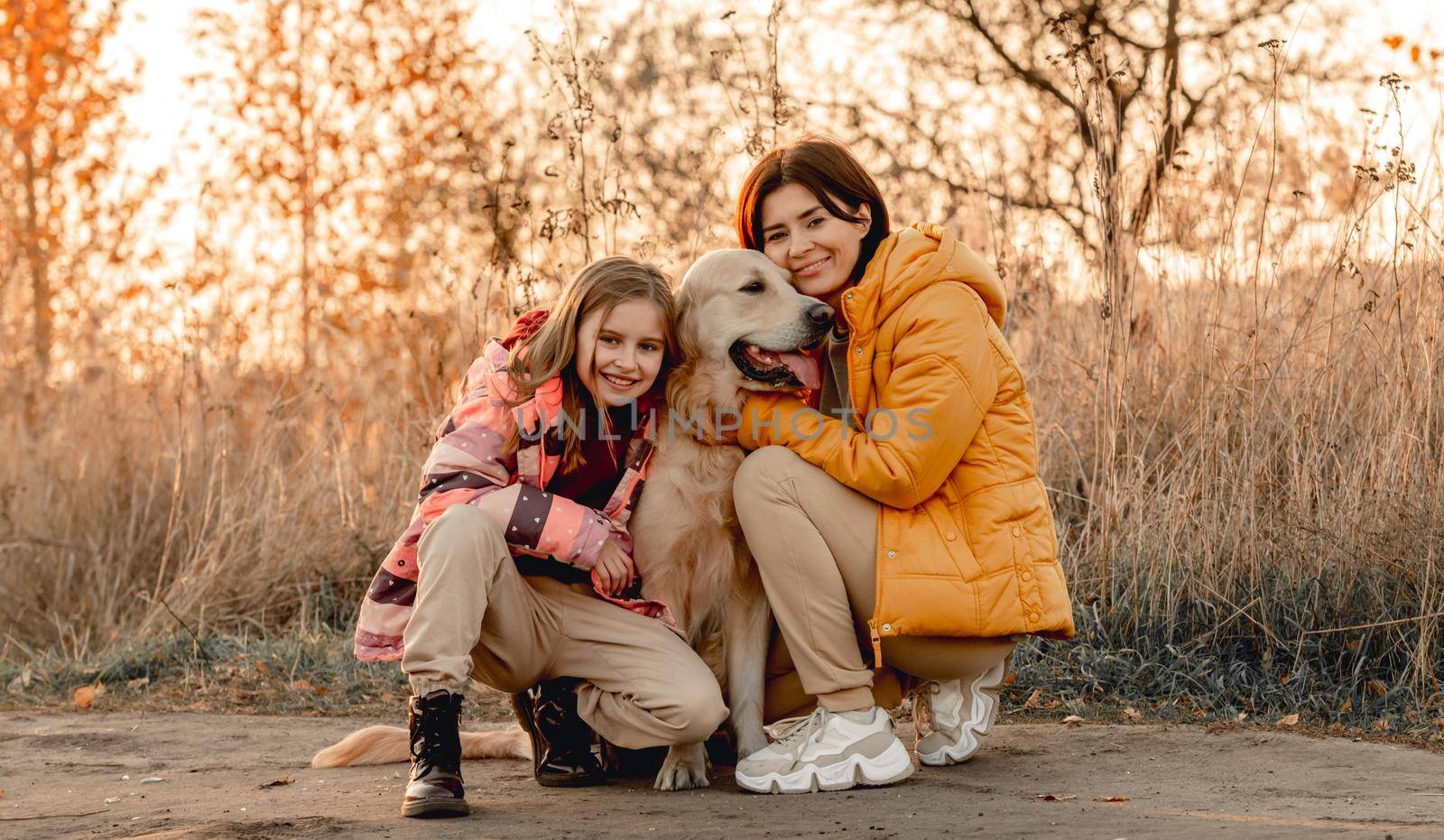 Family with golden retriever dog with sunset light outdoors. Mother girl and daughter child with doggy pet labrador at nature at autumn