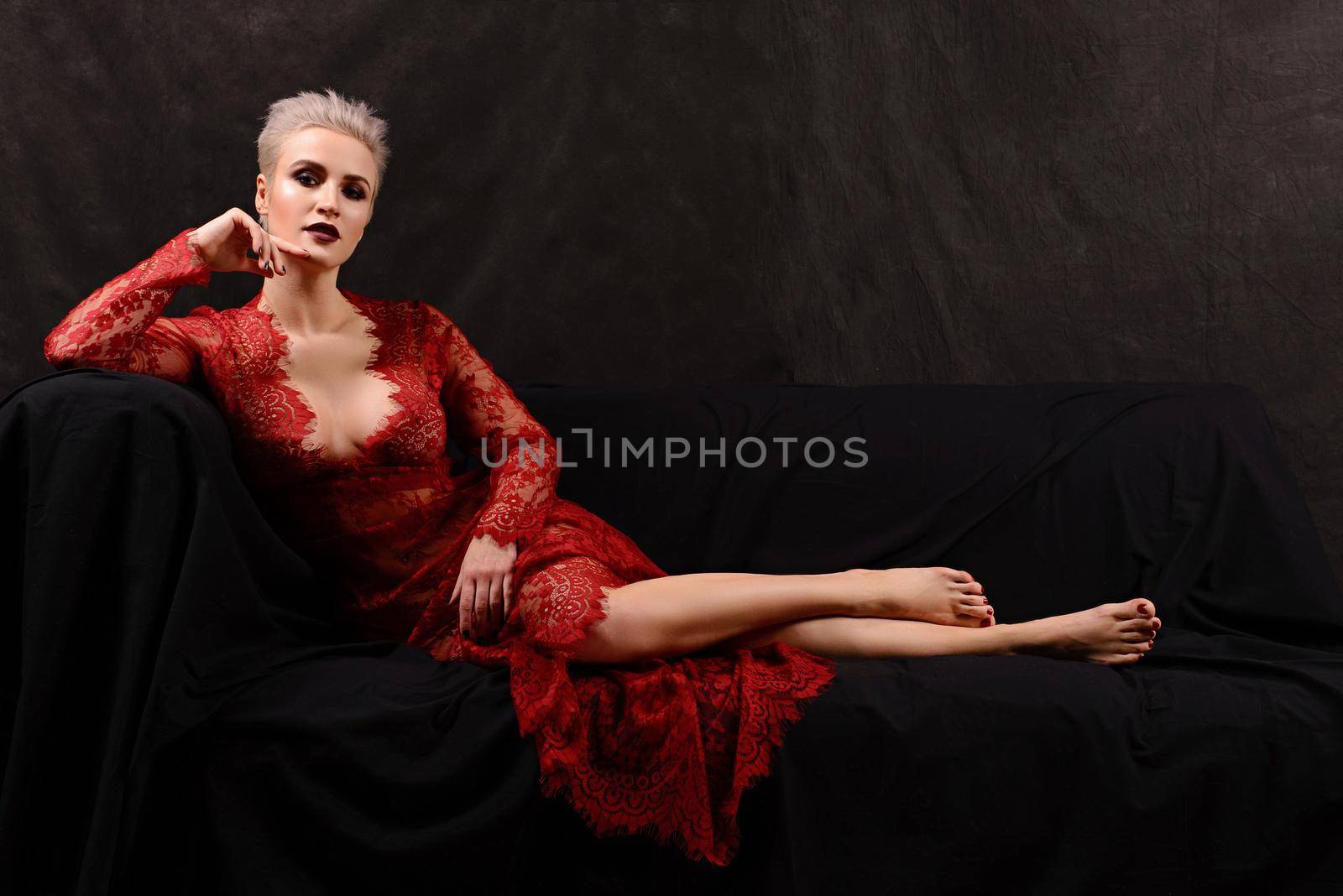 insanely beautiful short-haired young blonde woman in red lace dress lying on the couch.