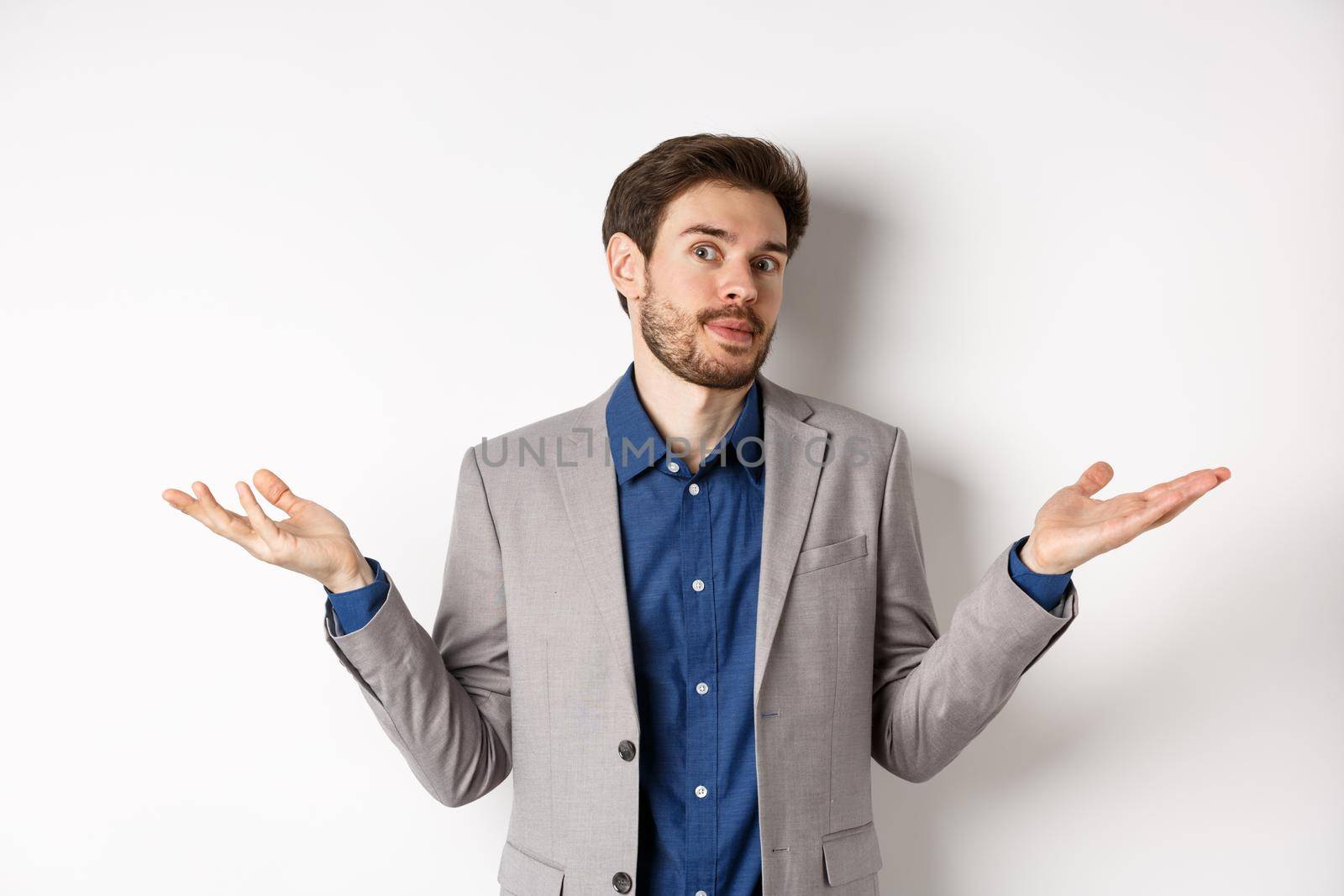 I dont know. Clueless bussiness man in suit shrugging shoulders and looking unaware, have no idea, standing on white background.