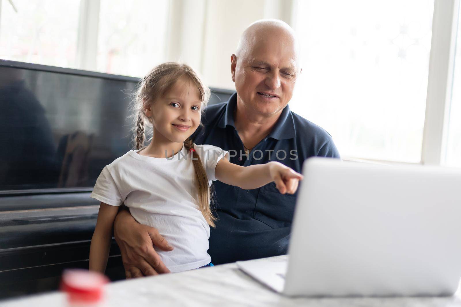 Senior grandfather with small granddaughter indoors sitting at table.