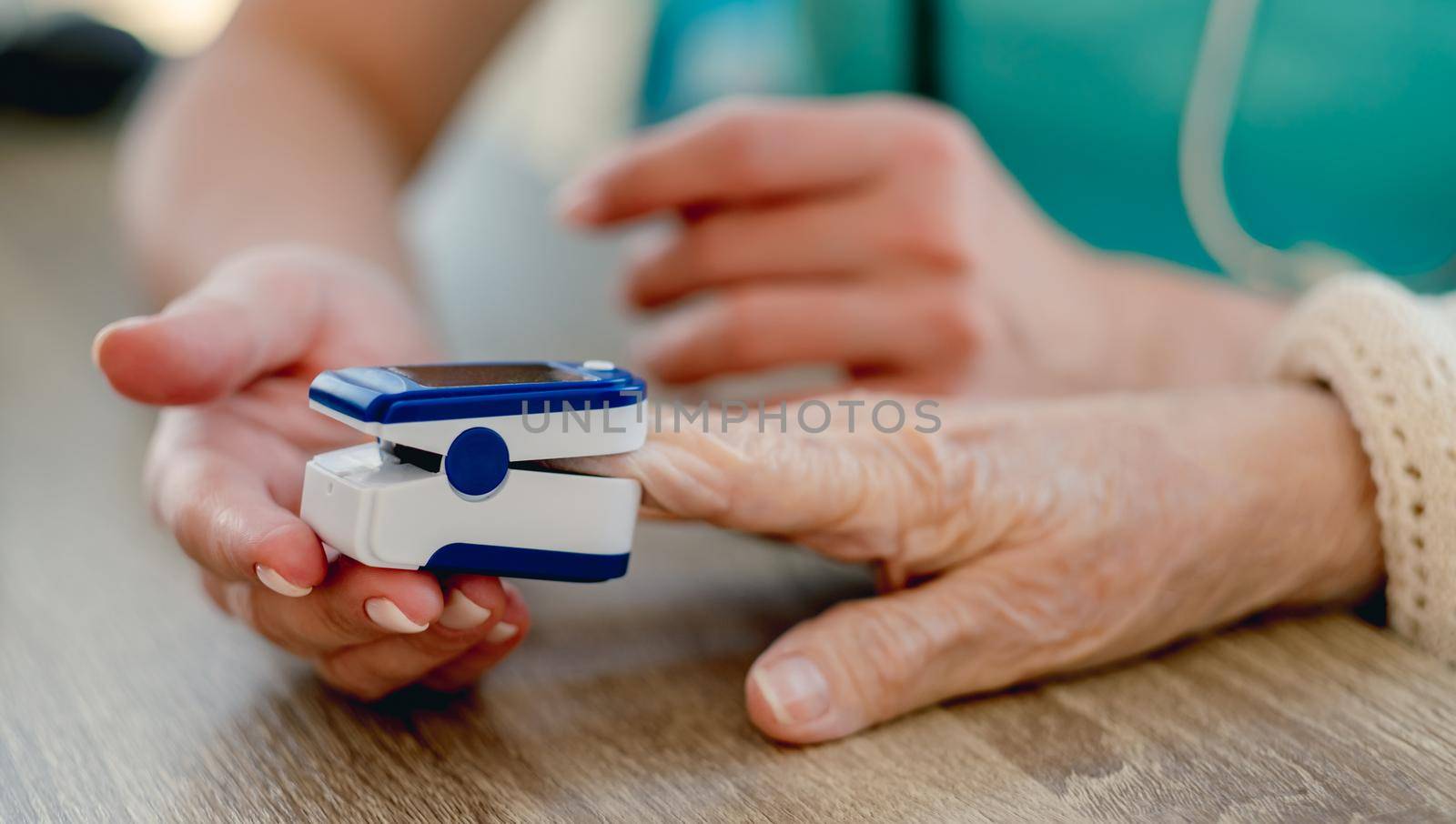 Doctor using pulse oximeter on old woman hand during appointment in clinic