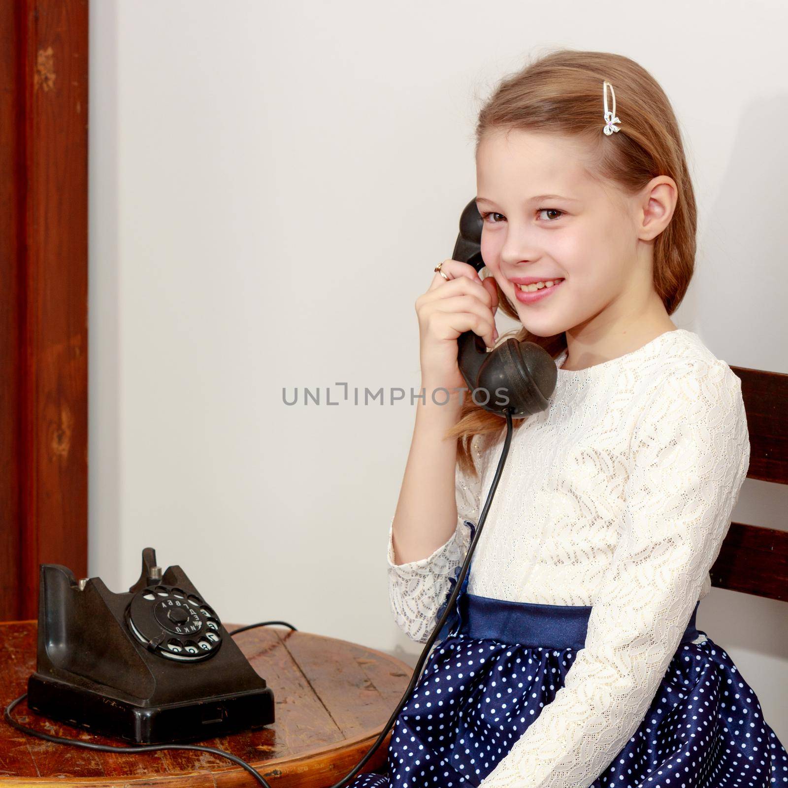 Cheerful little girl talking on a vintage telephone in the interior of the sixties of the last century.Retro style.