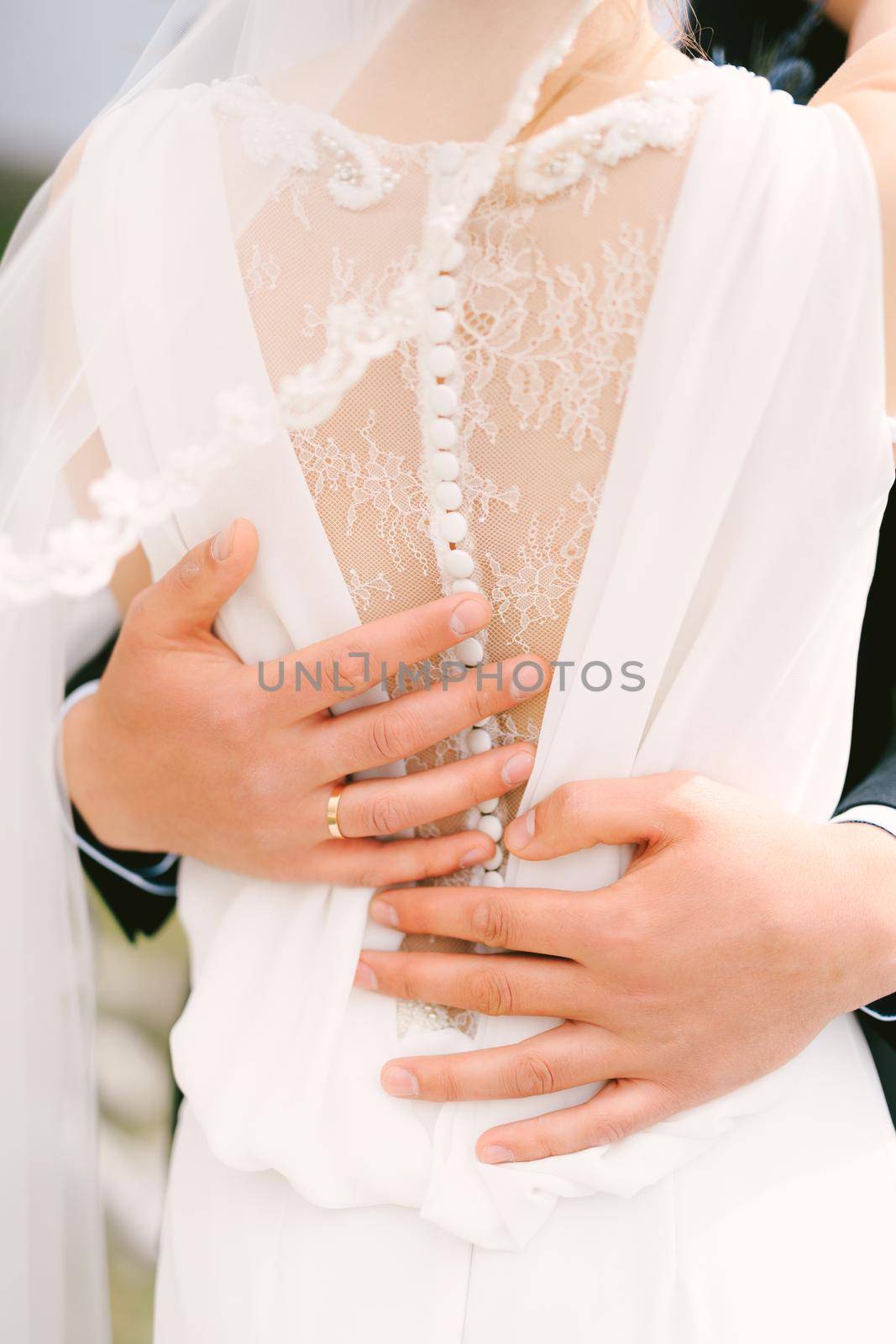 Hands of the groom hug the waist of the bride in a white lace dress. Close-up. Back view by Nadtochiy
