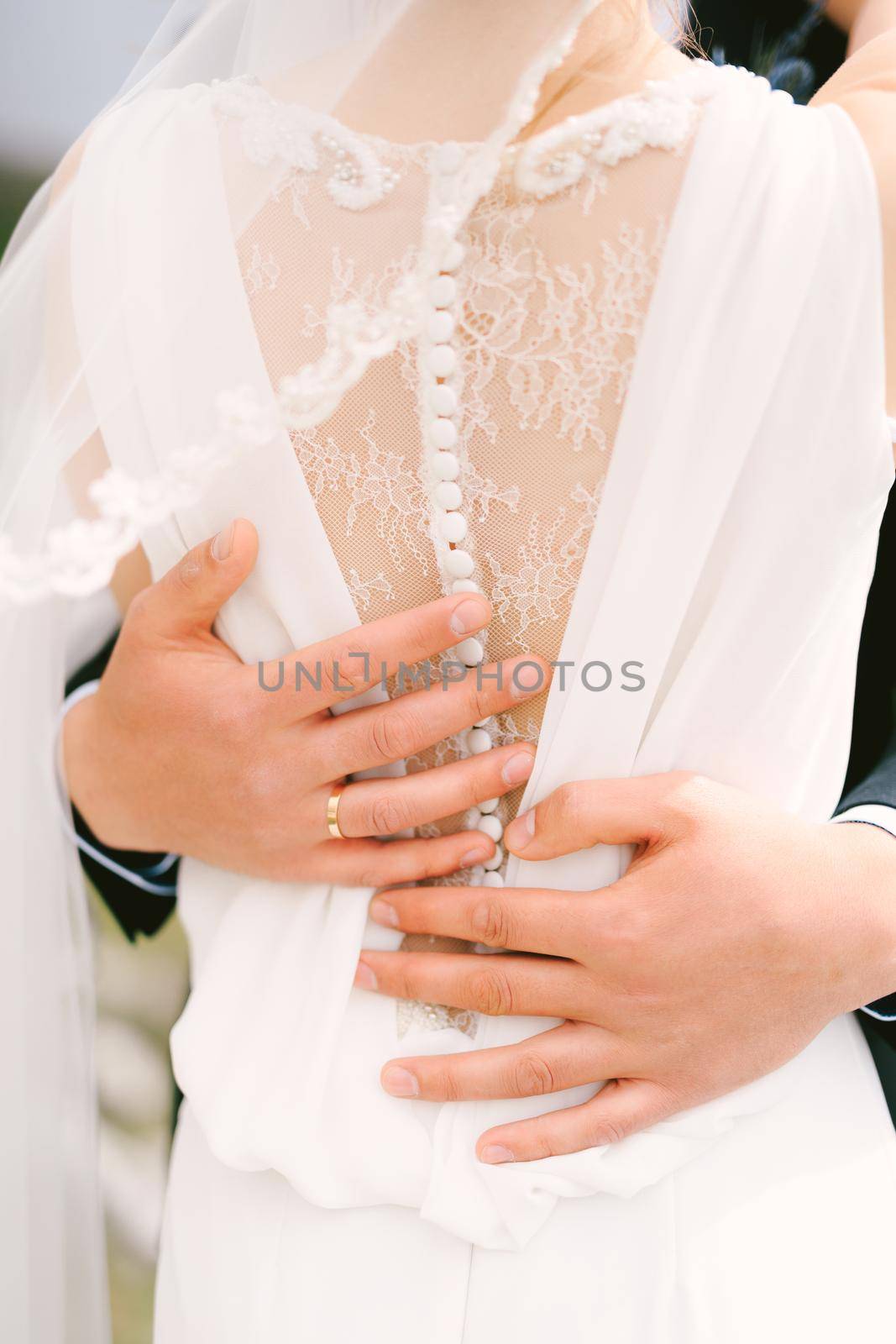 Hands of the groom hug the waist of the bride in a white lace dress. Close-up. Back view. High quality photo
