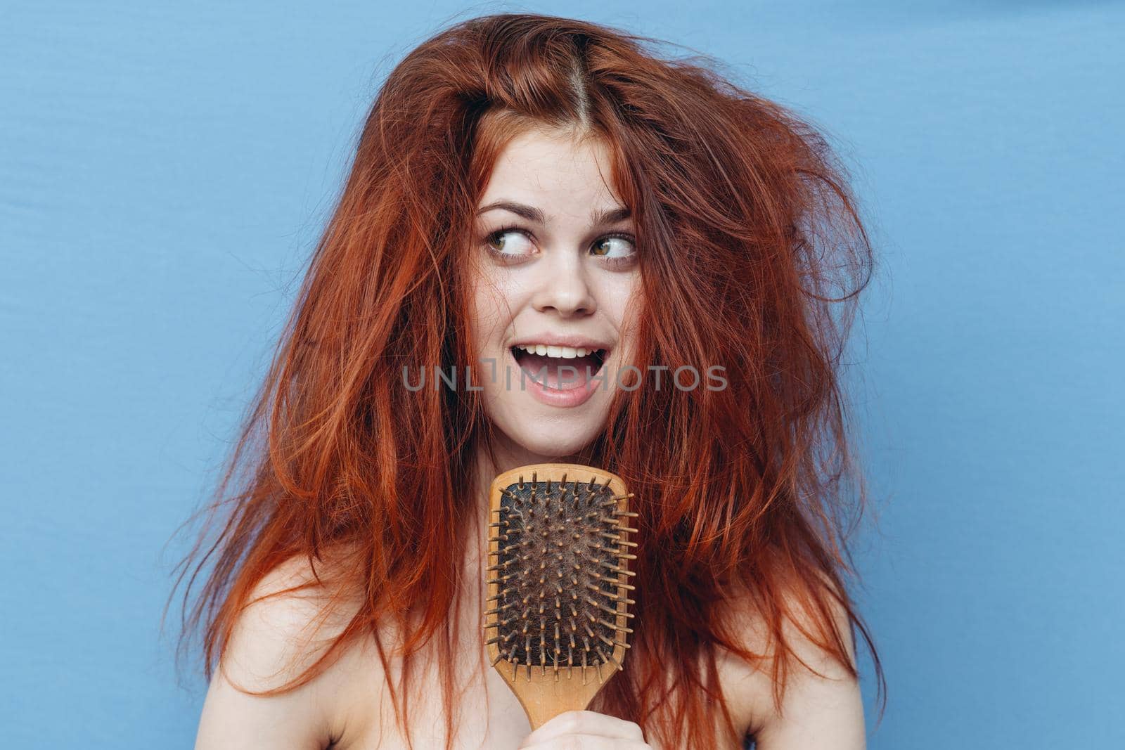 woman with bare shoulders tousled red hair comb blue background. High quality photo