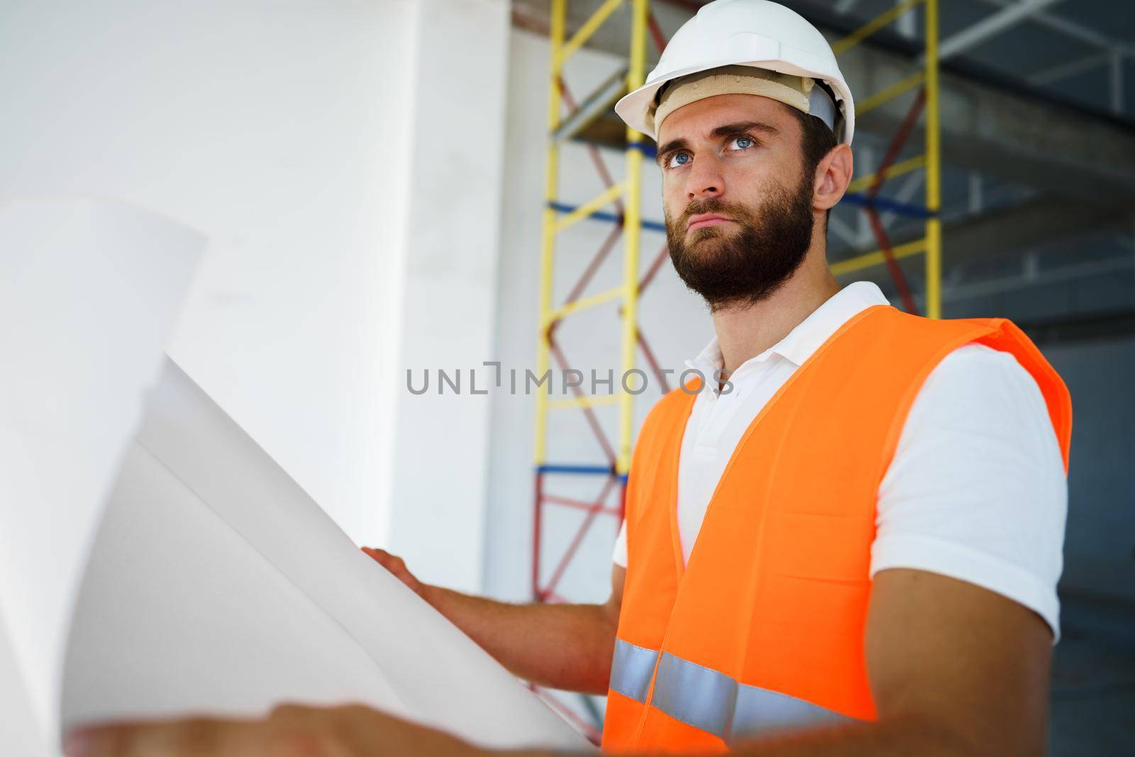 Builder or architect in hardhat supervising a project, looking at blueprints, close up