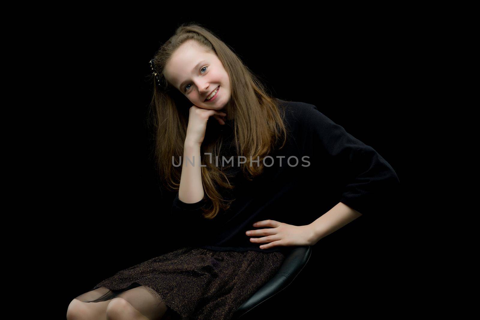 Girl teenager sitting on a chair in the studio on a black background. The concept of style and fashion.