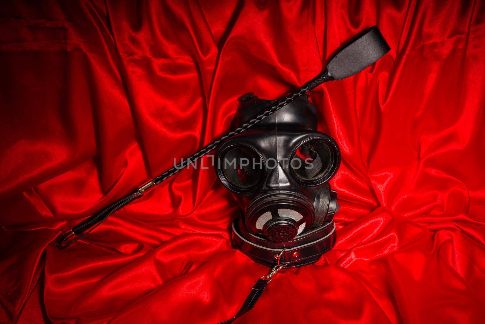 Close up bdsm outfit. Bondage, kinky adult sex games, kink and BDSM lifestyle concept with gas mask, whip, collar on red silk with copy space.