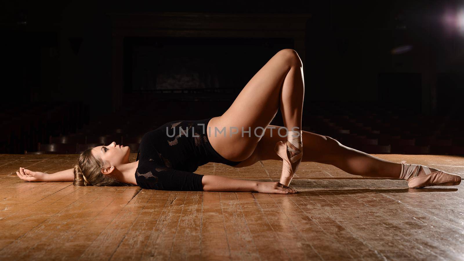 Pretty ballerina in pointe shoes is lying on his back bent leg on the stage