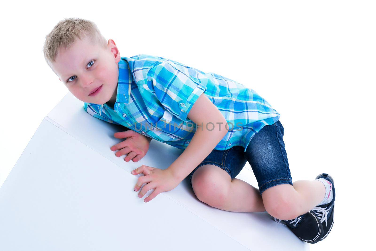 Cute little boy posing near a white cube. The concept is a happy childhood, the development of the child. Studio photography isolated on a white background.