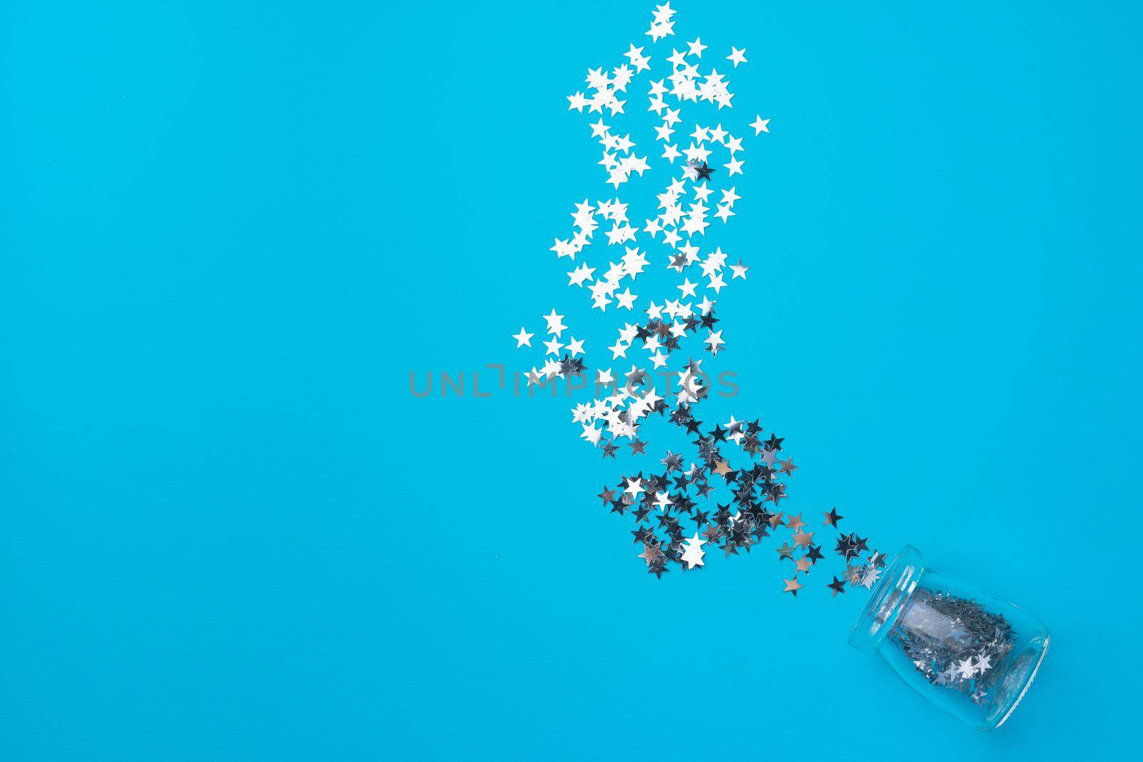 Glass jar with scattered confetti on blue background top view