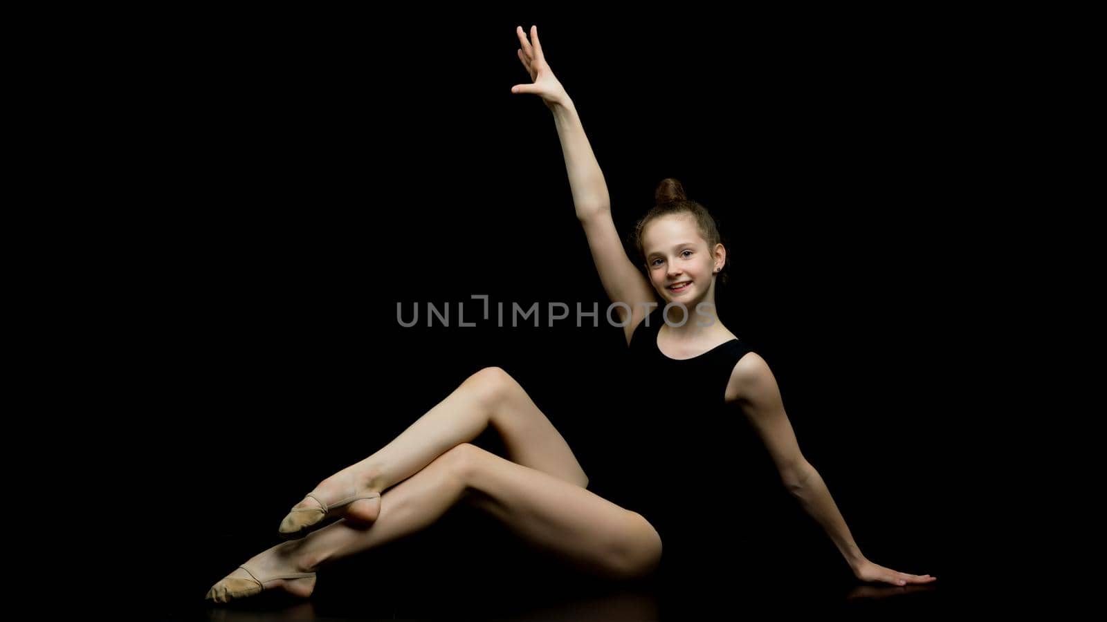 Beautiful girl gymnast performs gymnastic exercise in a photo studio on a black background. The concept of sports, a healthy lifestyle