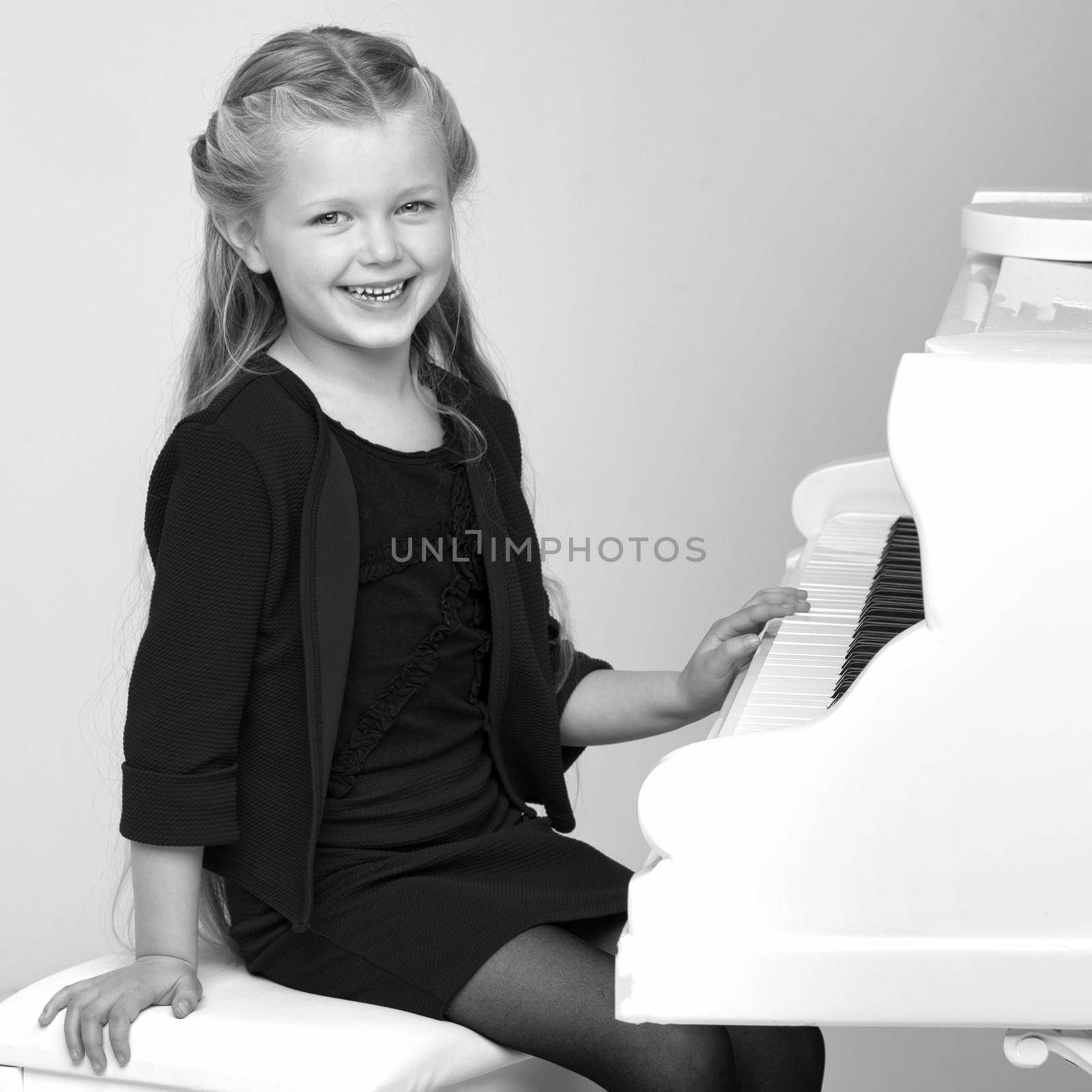 Beautiful little girl playing on white grand piano. Black and white shot of pretty long haired girl sitting at piano in living room. Cute child learning to play music instrument