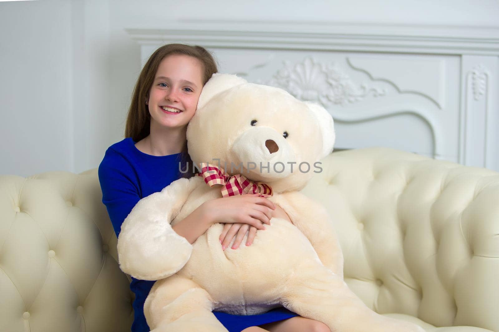 A teenage girl of school age is sitting on the couch with a big teddy bear. The concept of a happy childhood.