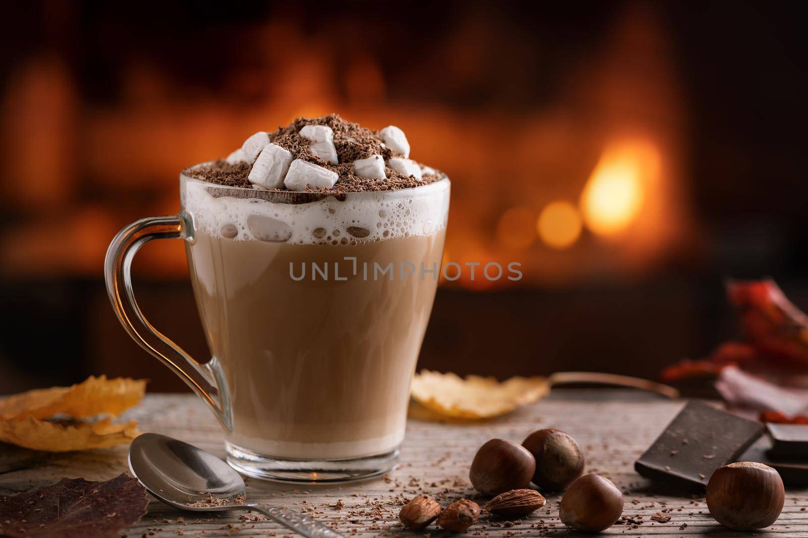 Cocoa with marshmallows and chocolate in a glass mug on a wooden table near a burning fireplace by galsand