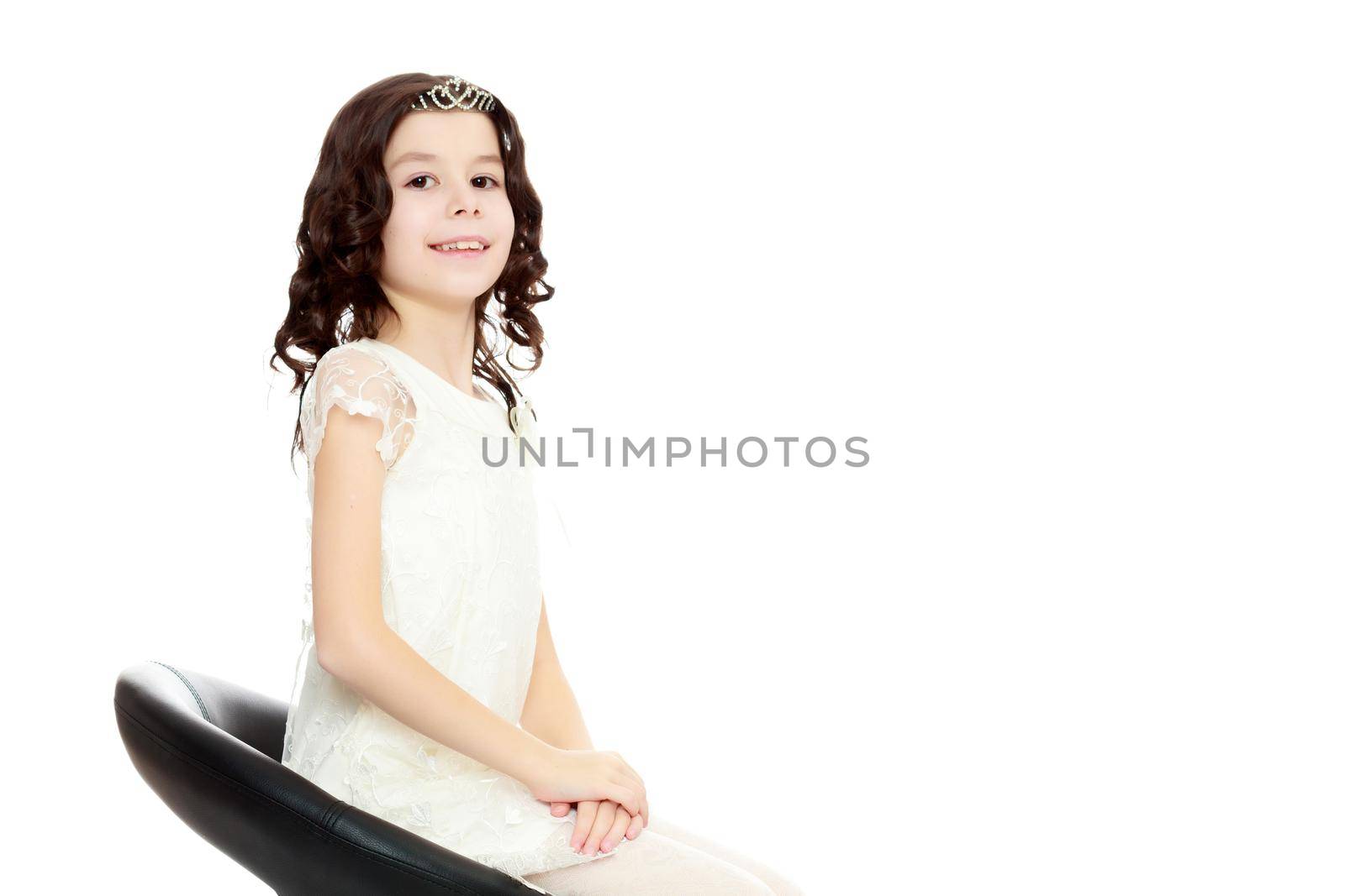 Adorable little girl with long, dark curly hair , in a long white beautiful dress. Girl sitting on a revolving chair. Close-up.Isolated on white background.