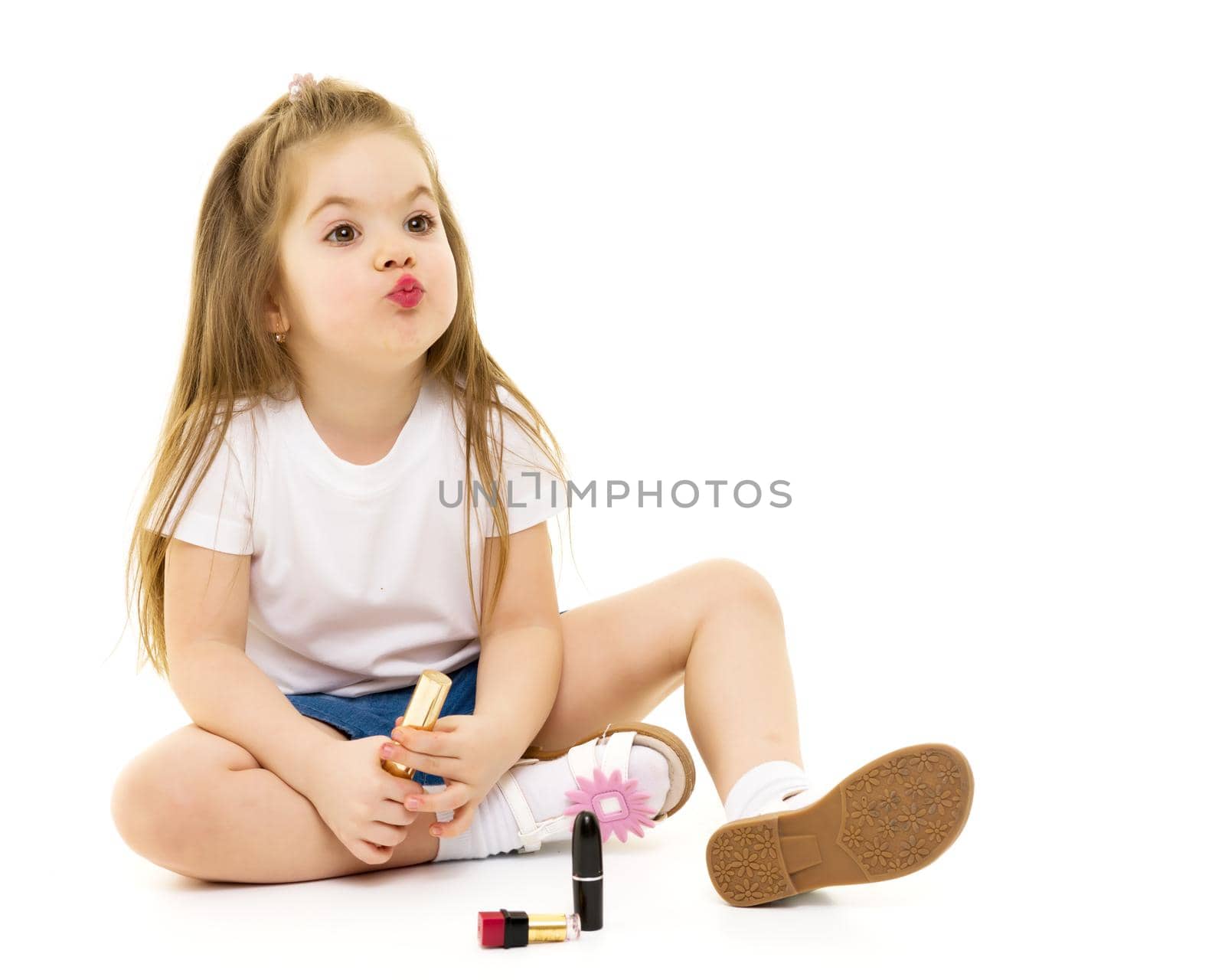 Cheerful little girl paints lips with mom's lipstick. The concept of beauty and fashion, family, advertising. Isolated on white background.