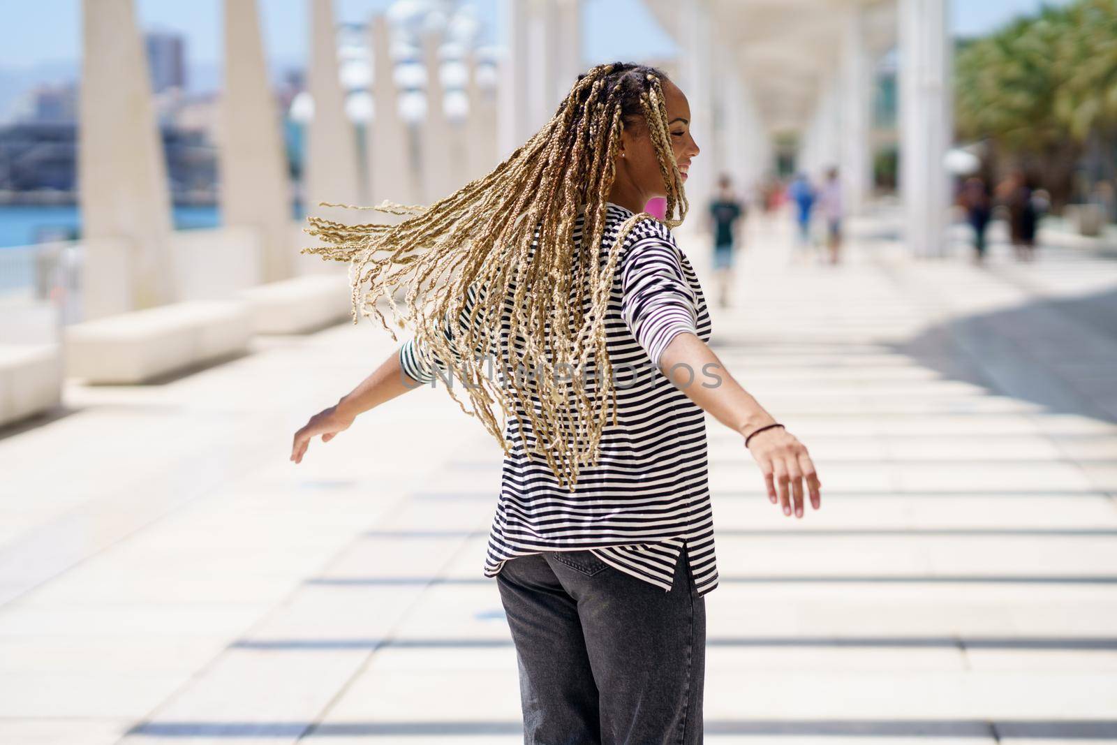 Young black female moving her coloured braids in the wind. Typical African hairstyle. by javiindy