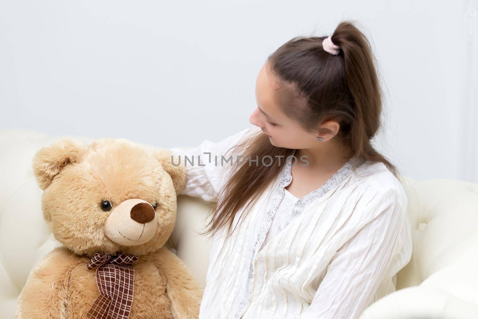 Beautiful little girl schoolgirl embraces with a teddy bear. The concept of a happy childhood, children's emotions.