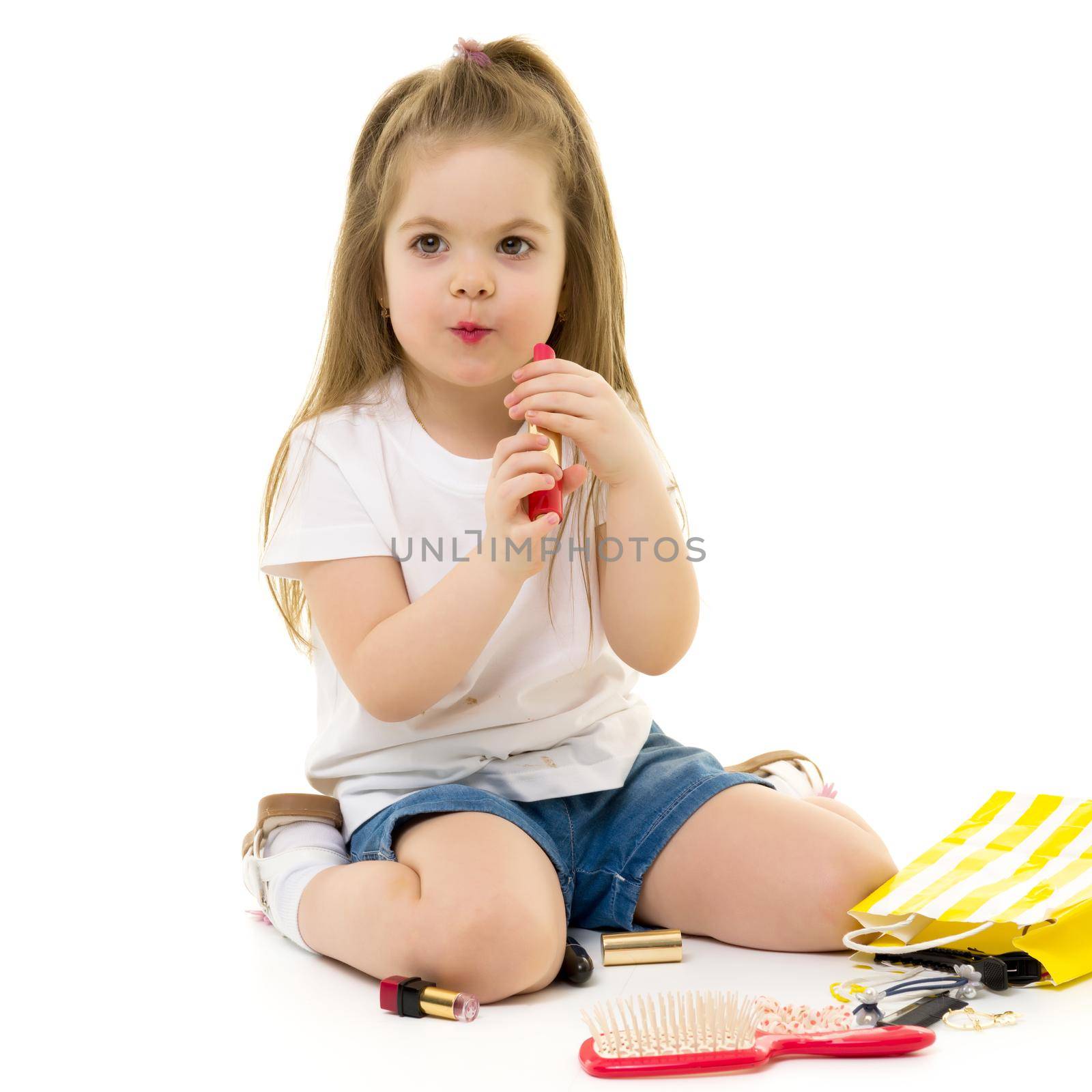 Cheerful little girl paints lips with mom's lipstick. The concept of beauty and fashion, family, advertising. Isolated on white background.