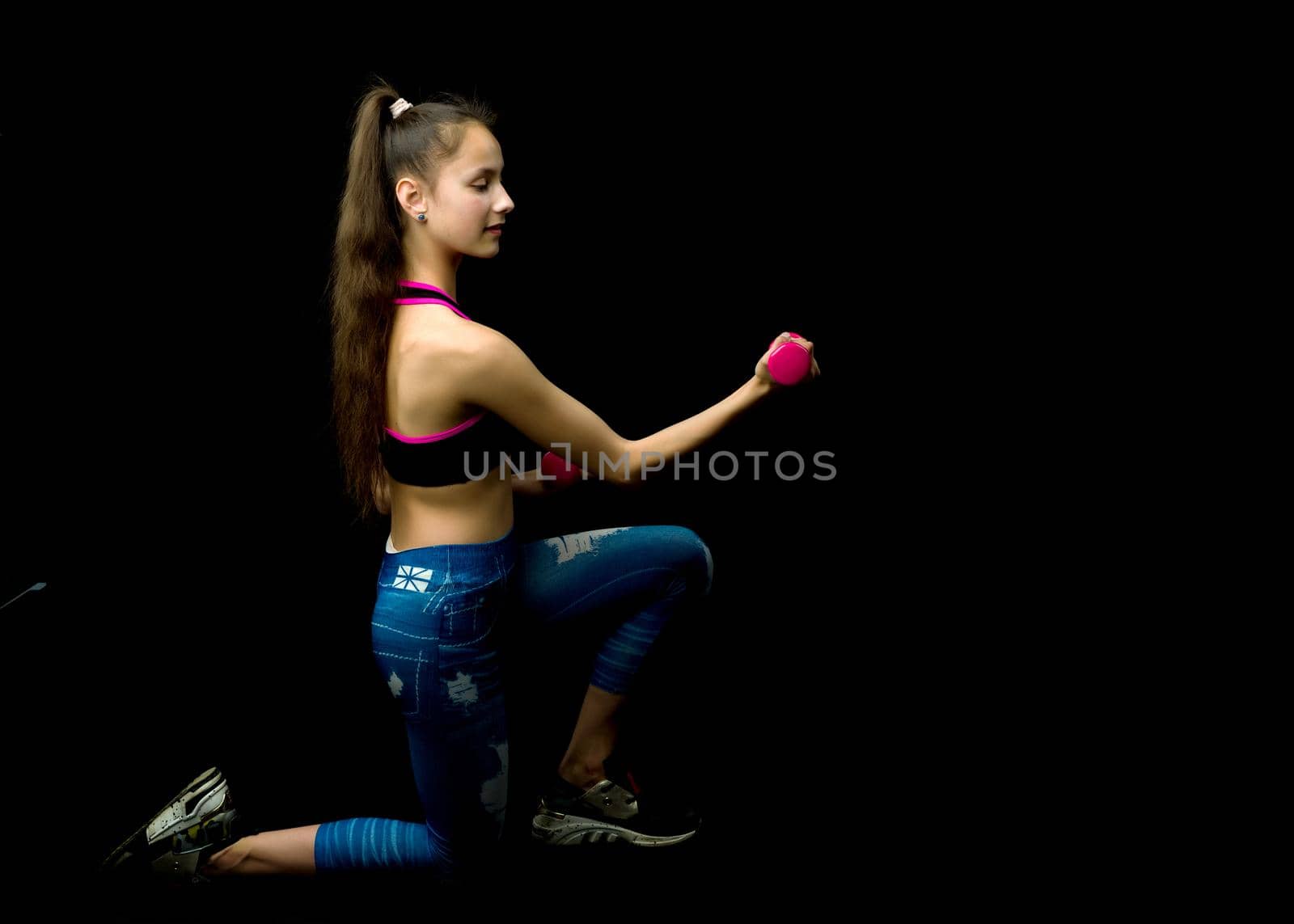 A teenage girl with dumbbells in her arms performs exercises in the fitness club. The concept of sport and a healthy lifestyle of the younger generation. Isolated