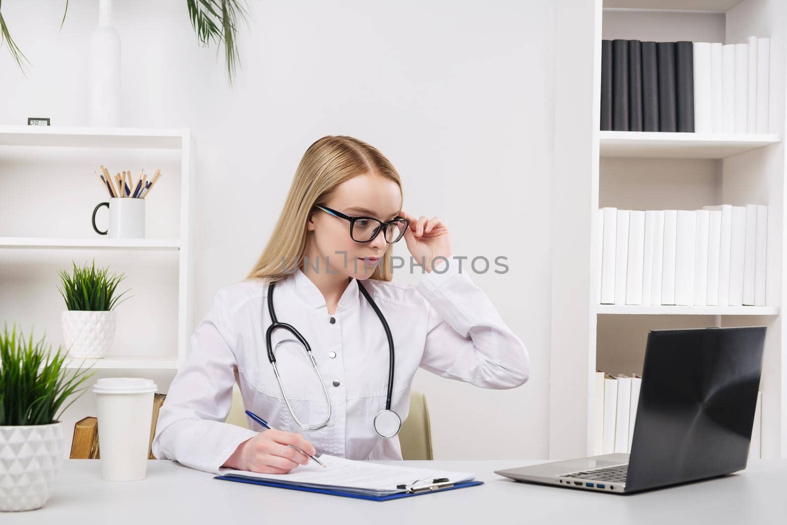 Young beautiful doctor woman working happy and smile in hospital, sitting on table, medical concept
