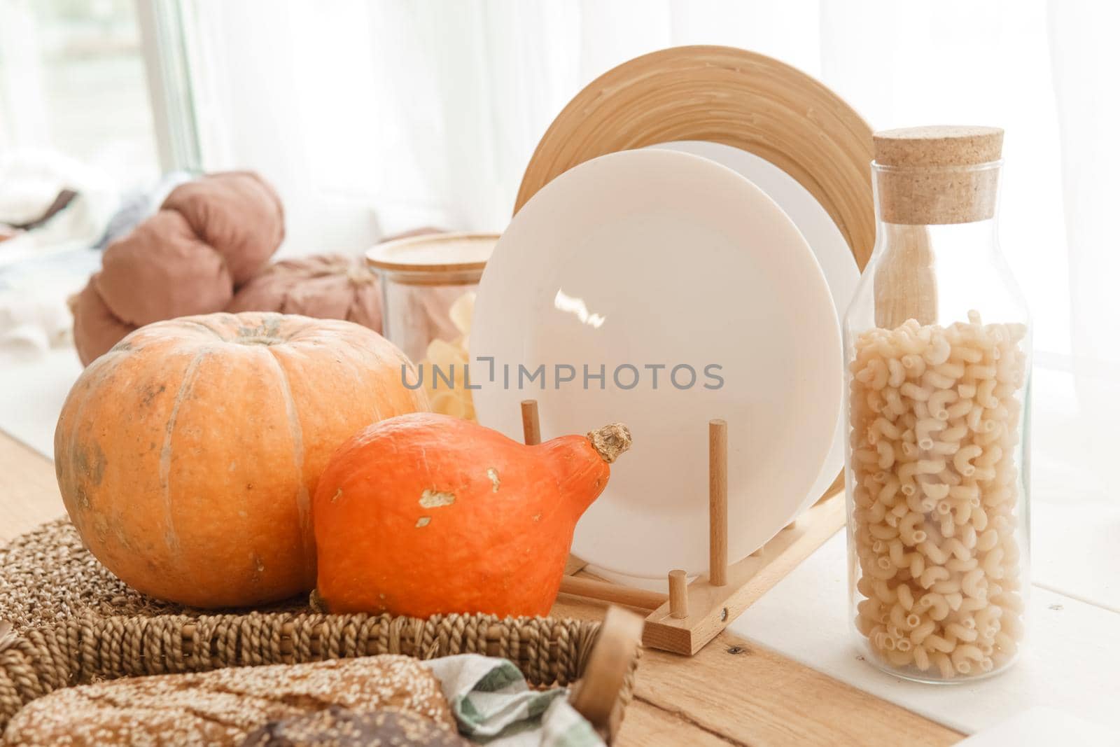 Kitchen countertop by the window in a bright room. Orange pumpkins, bread and pasta on the countertop. Autumn mood at home.