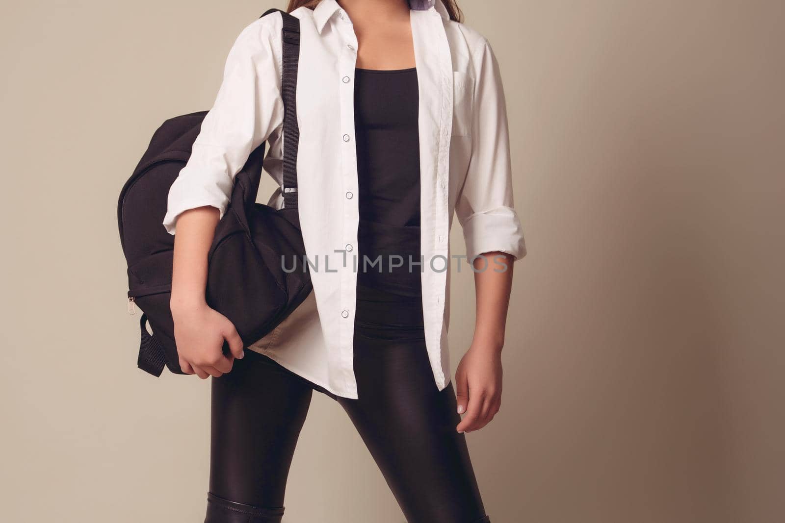 Beautiful blonde girl wearing a white shirt with a leather backpack on her back, on a gray background, shooting in the studio