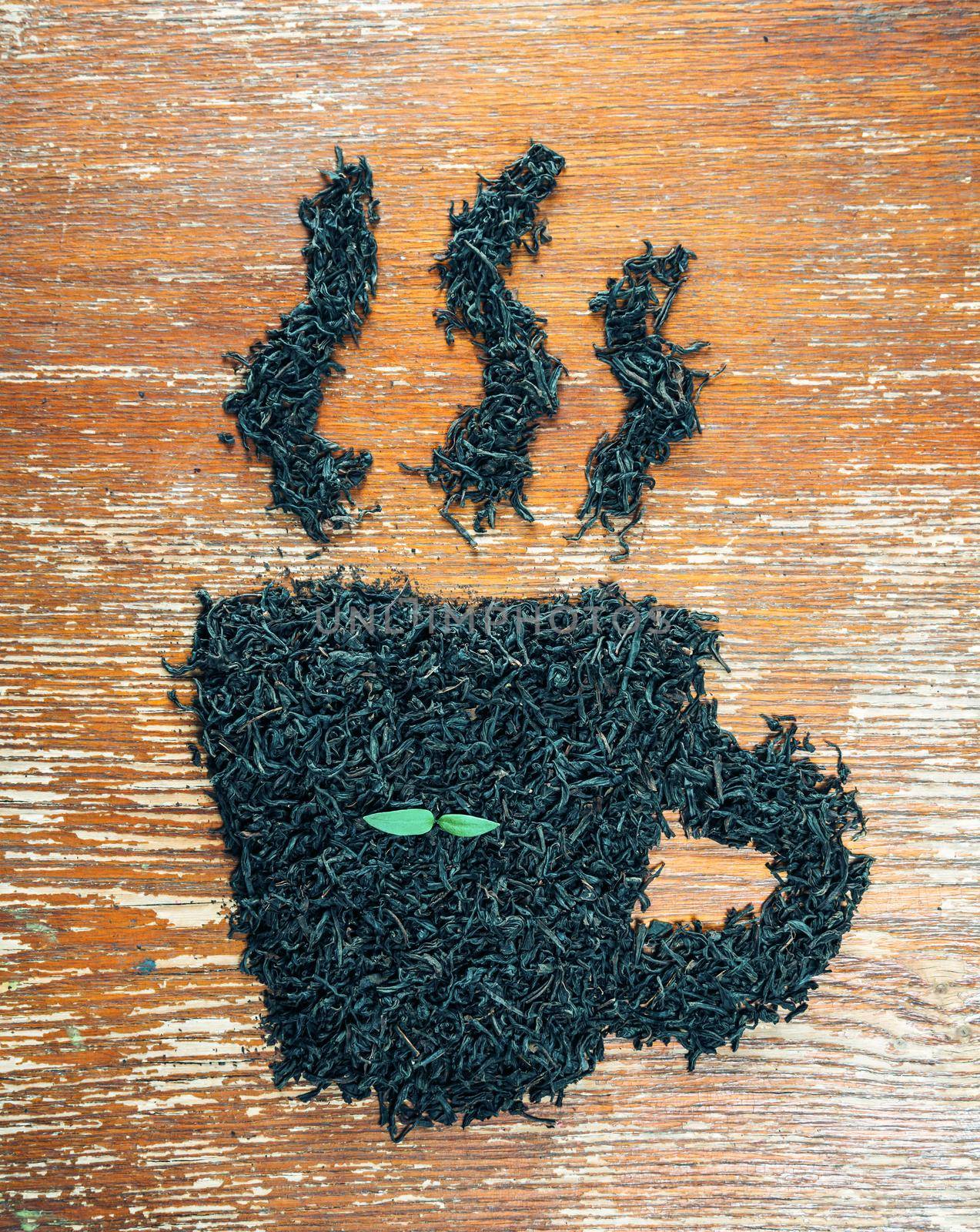 Black leaf tea in the shape of cup with green plant on a wooden table