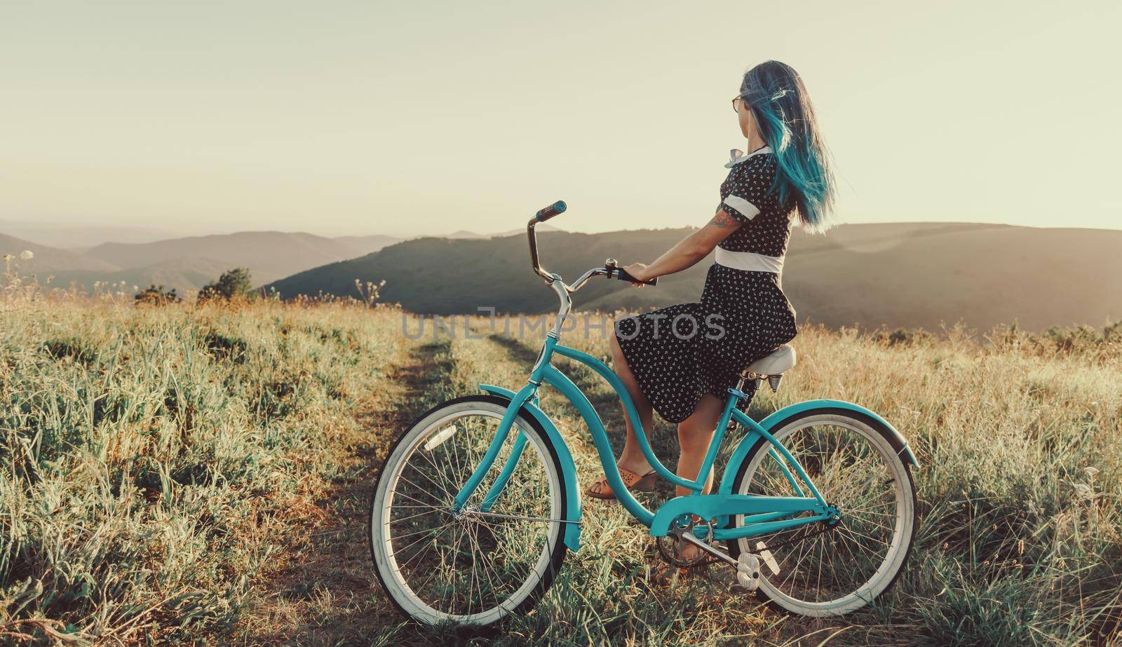 Beautiful young woman wearing in dress sitting on cruiser bicycle and looking into the distance outdoor.