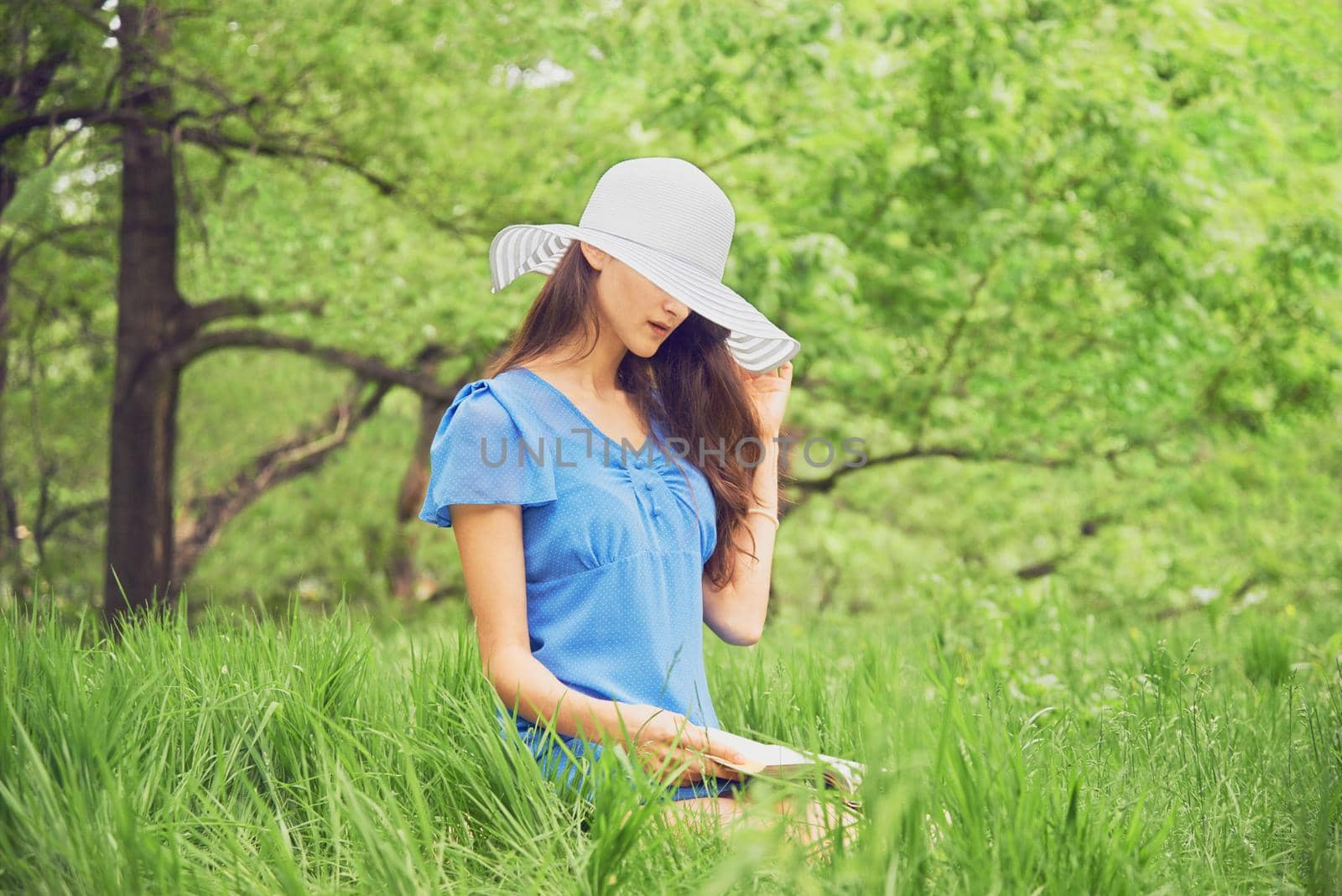 Beautiful woman in a hat with wide brim reads a book in summer park