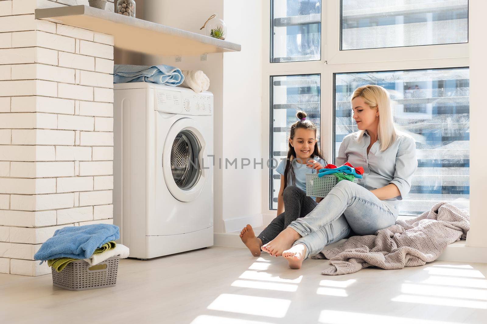 Happy housewife and her daughter with linen near washing machine by Andelov13