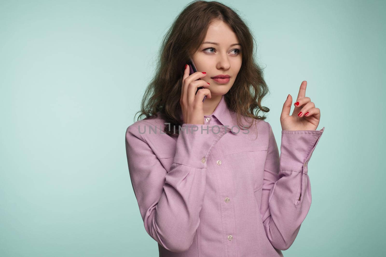 beautiful caucasian surprised young girl talking on her cell phone pointing up isolated background - Image