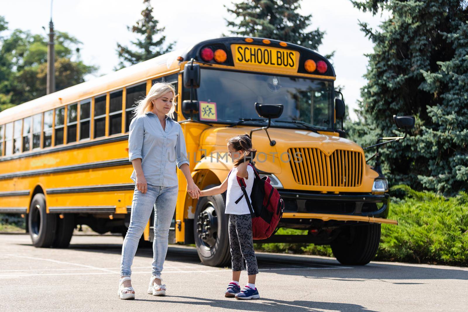 Mother escorts the schoolgirl with ponytails and a backpack to school.