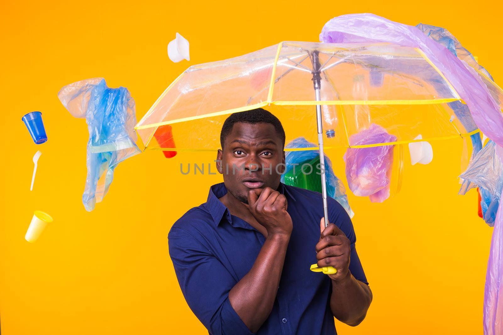 Problem of trash, plastic recycling, pollution and environmental concept - pensive african american man on yellow background with garbage
