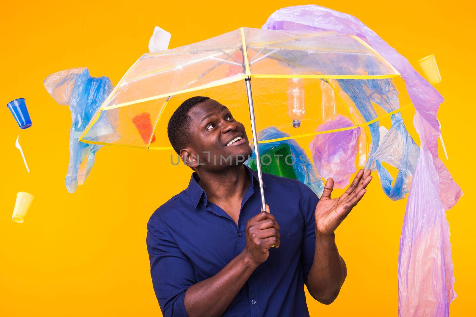 World Environment Day, plastic recycling problem and environmental disaster concept - Surprised african american man looking on trash on yellow.
