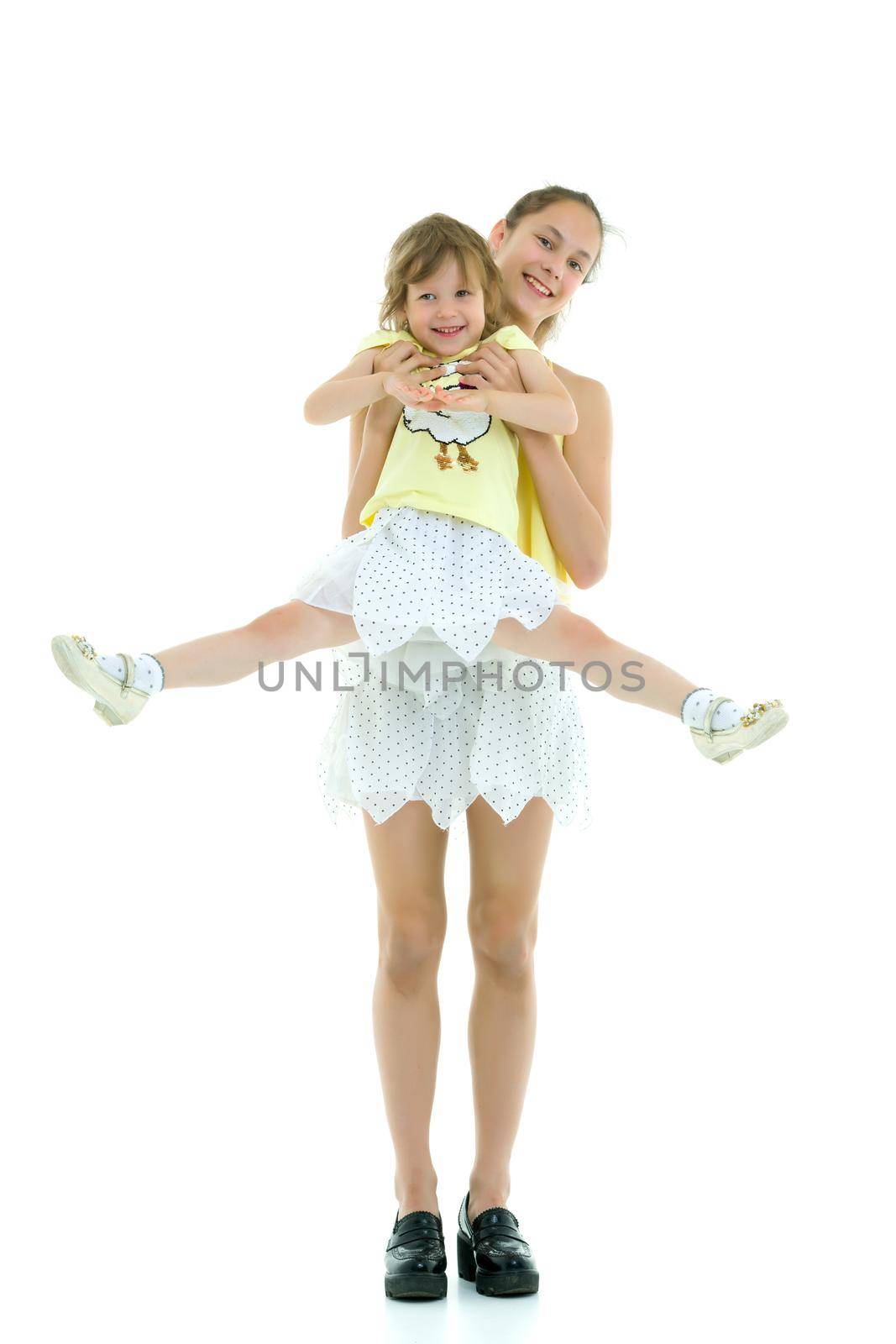 Beautiful young girl holding her little sister in her arms. by kolesnikov_studio